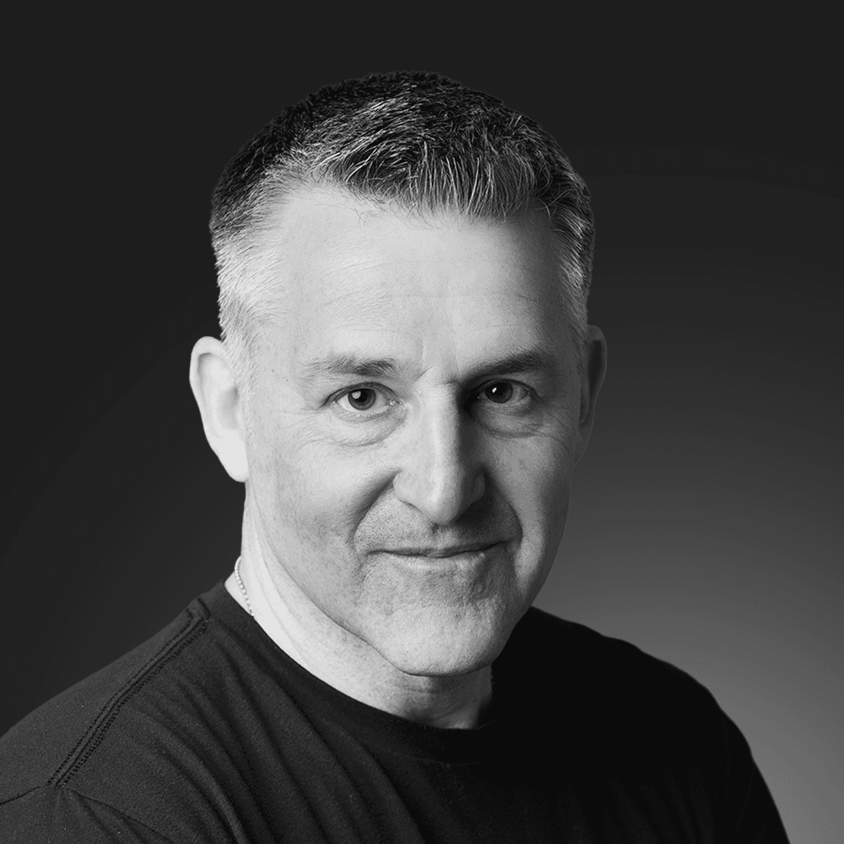 Smiling person with curly hair, wearing a black shirt, against a warm, dark background.