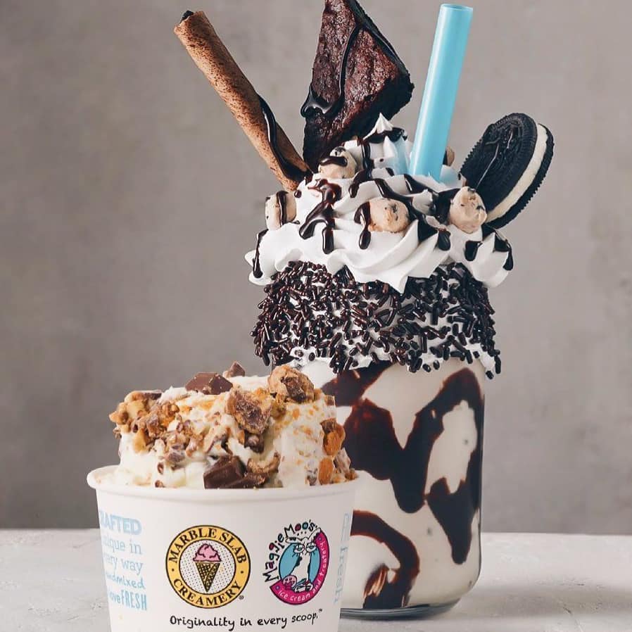 Loaded milkshake topped with a brownie, cookie, and chocolate sprinkles beside a cup of candy-studded ice cream