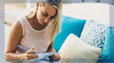 A woman relaxing on a couch outdoors and writing calmly in a notebook.