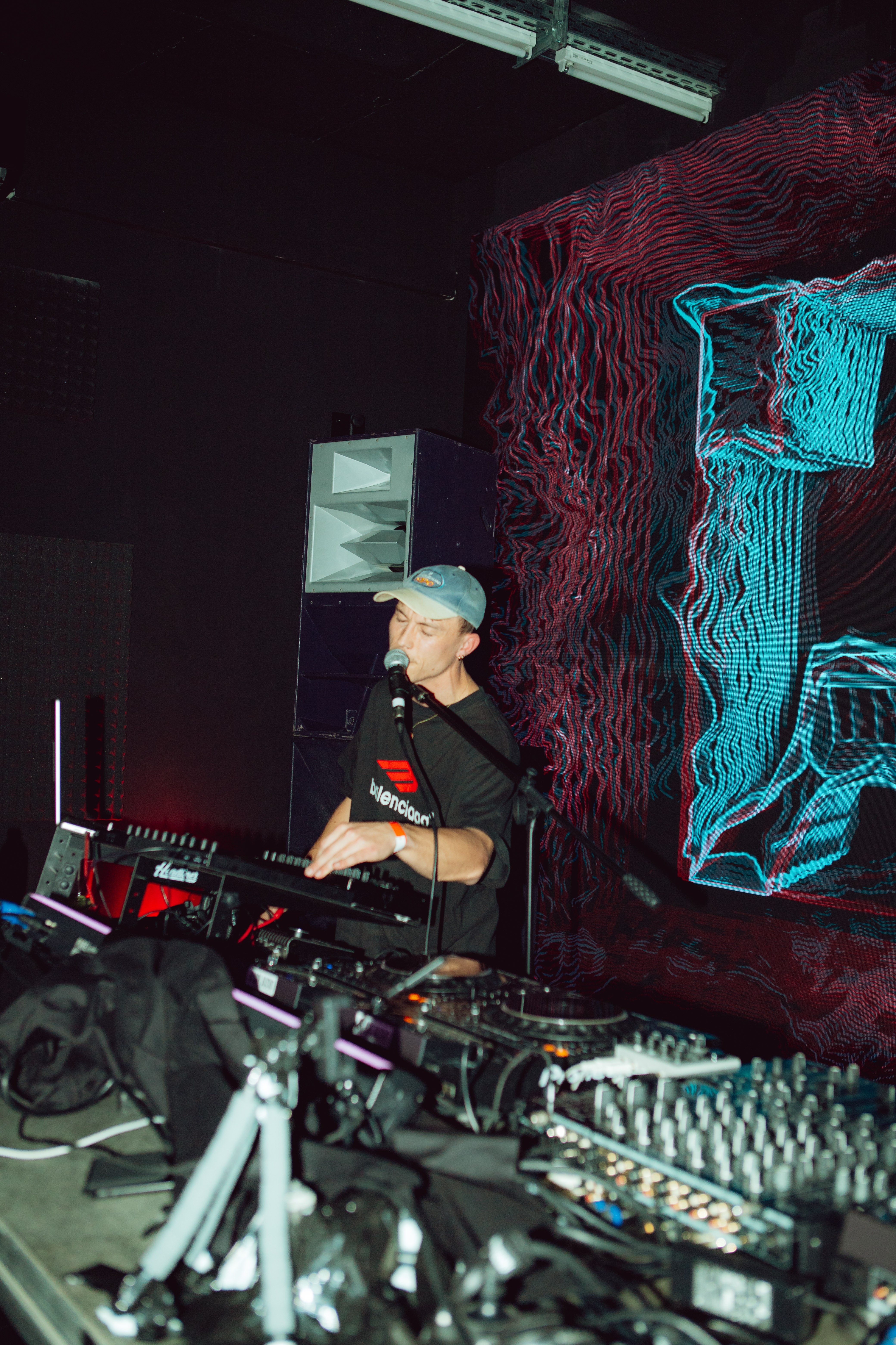 Electronic music performance in front of cyan and red projected linework at VOLLKOMMEN.