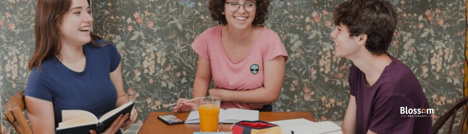 Three autistic adults sitting around a table reading books and engaging at one another