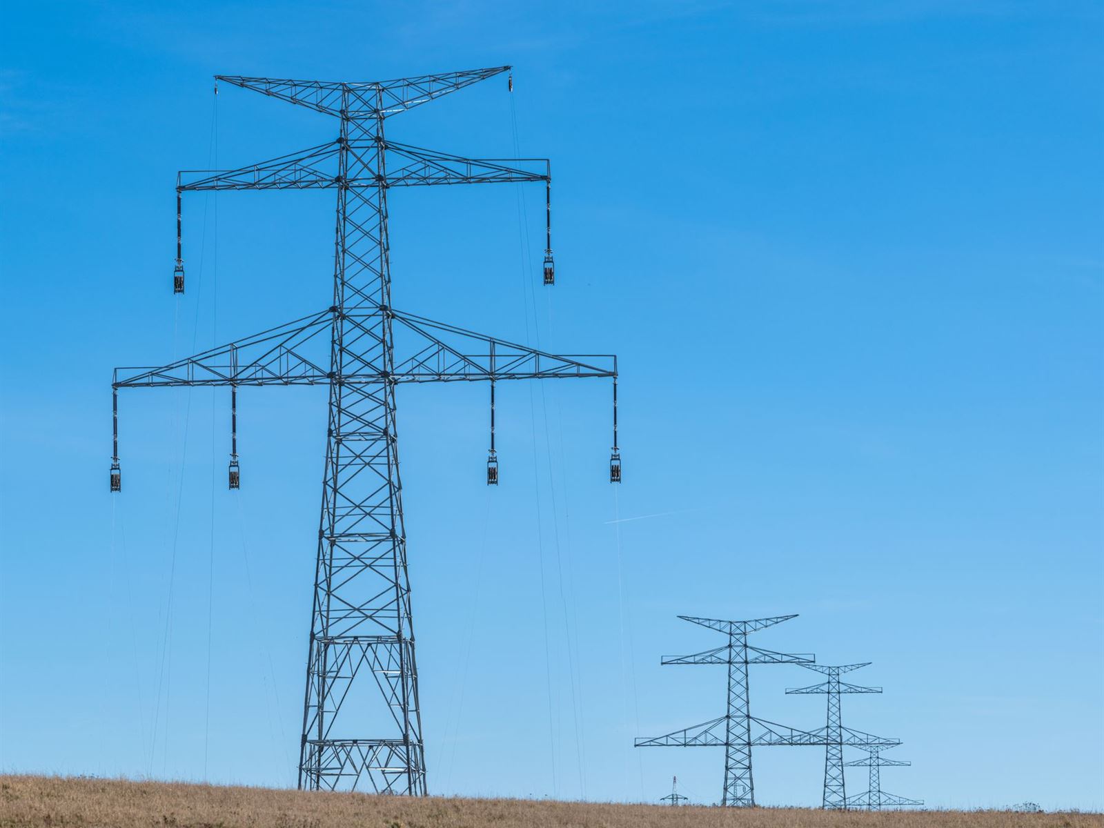 High-voltage transmission towers carrying power lines under a blue sky