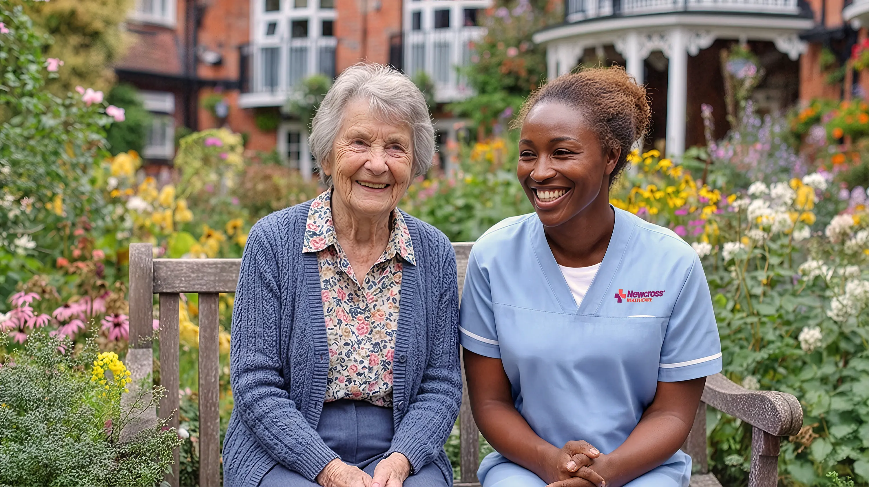 female newcross healthcare worker with elderly woman sitting in garden care home smiling