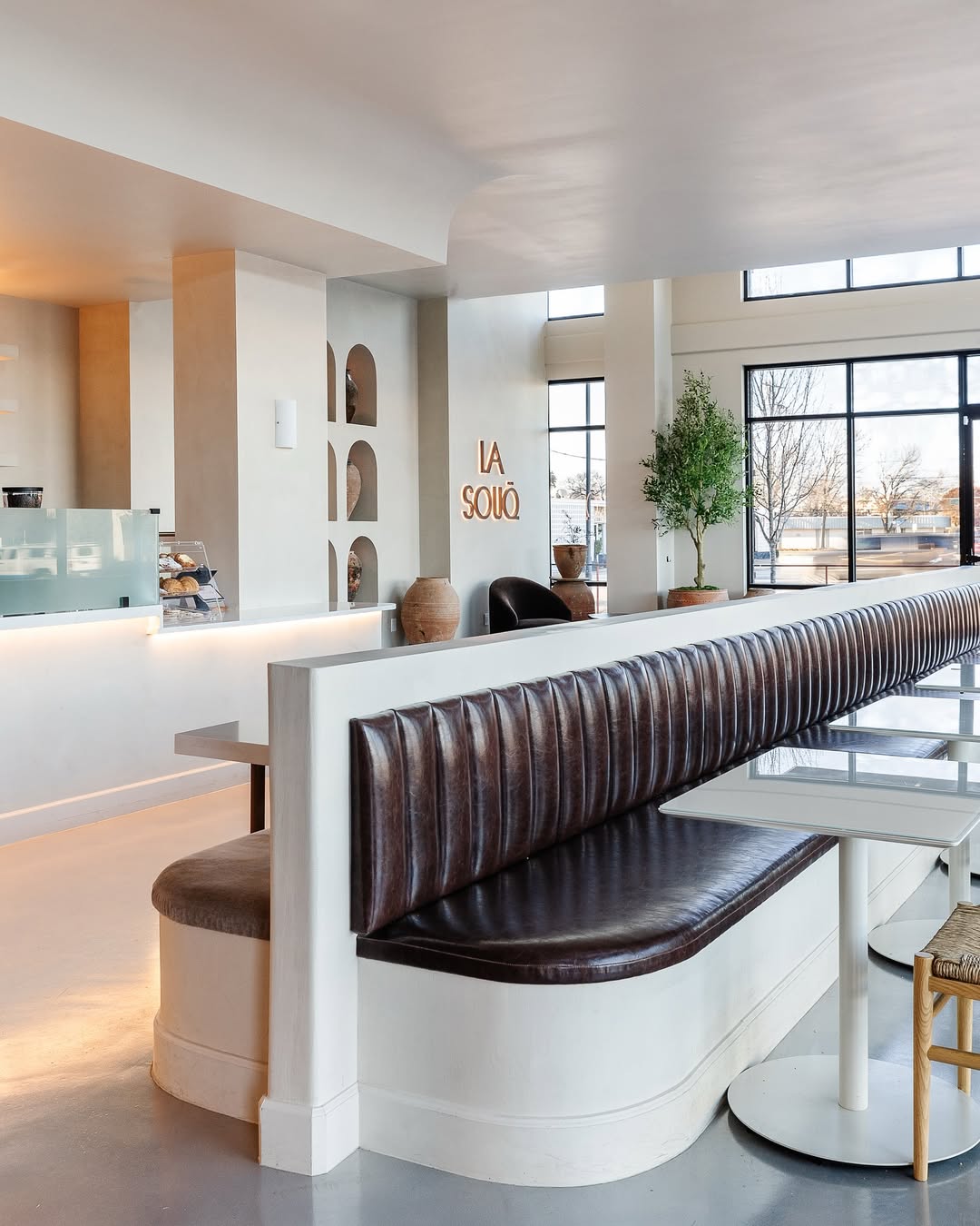 Interior seating area of La Souq café in Dallas featuring curved banquette seating, soft neutral finishes, arched wall niches, and illuminated La Souq wall signage in a calm, design-led space.