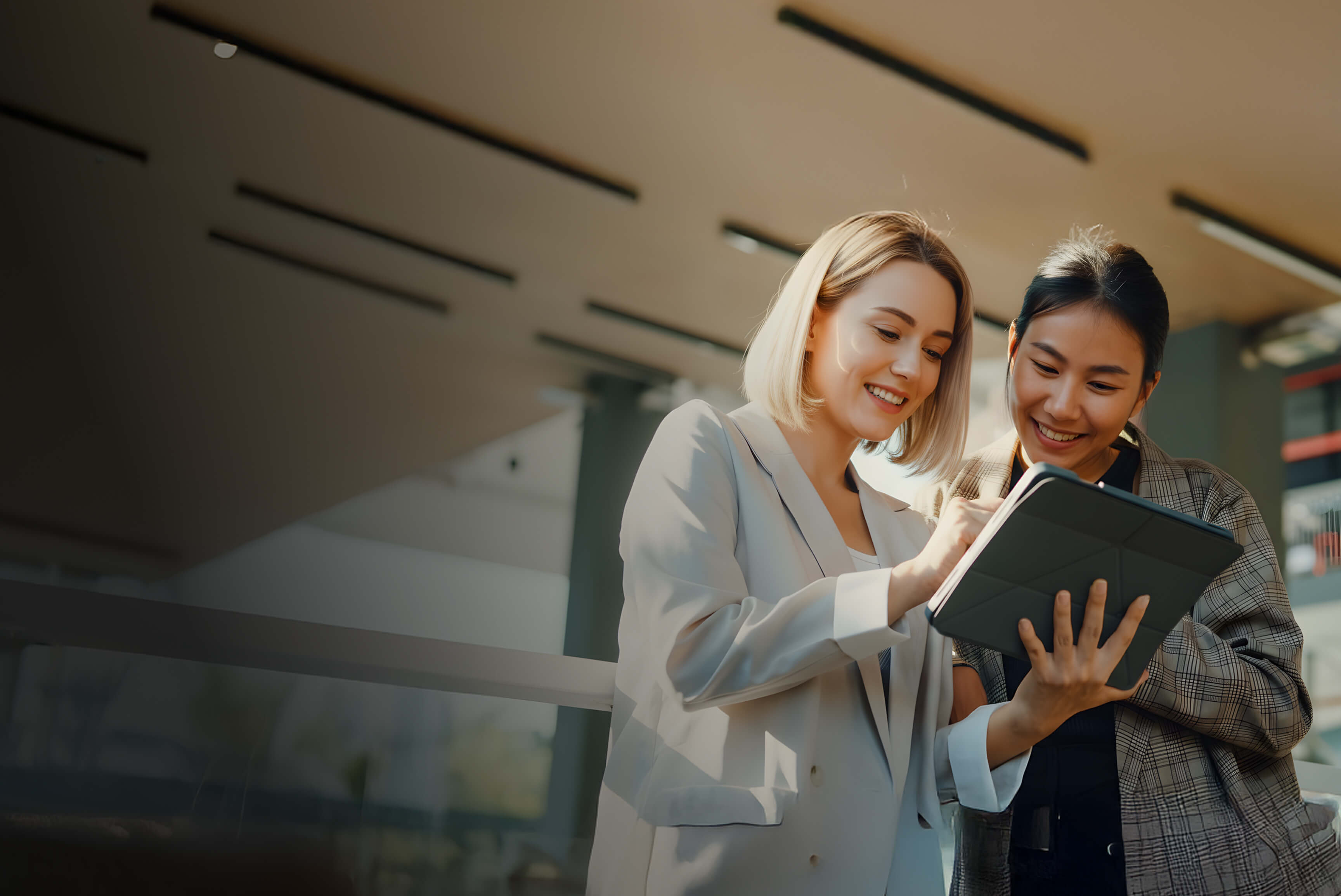 Two women in business suits looking at a tablet, likely discussing work or project details.