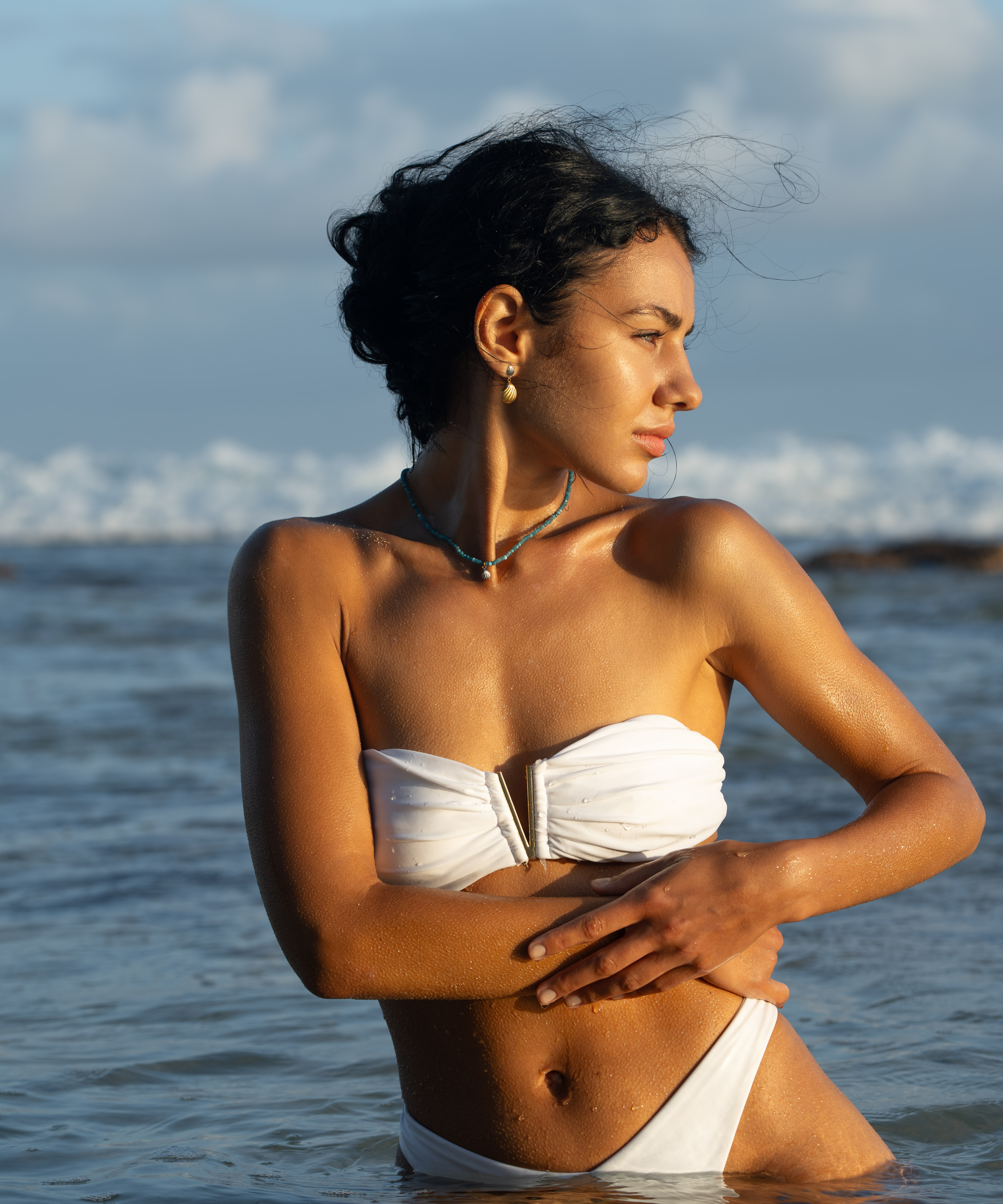 greek inspired jewelry worn by model standing in the ocean