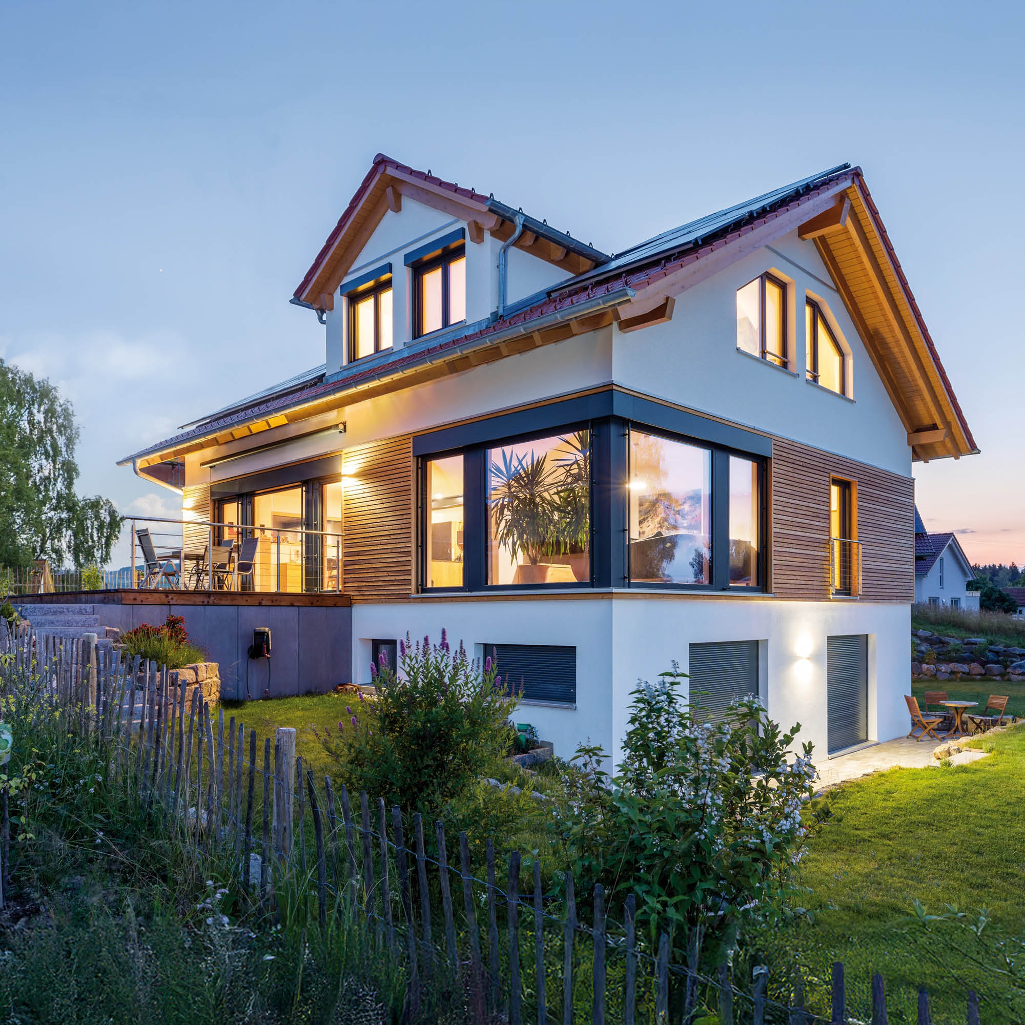 Modernes Einfamilienhaus in Abenddämmerung mit umliegendem Garten, Terrasse und Holzakzenten an der Fassade.
