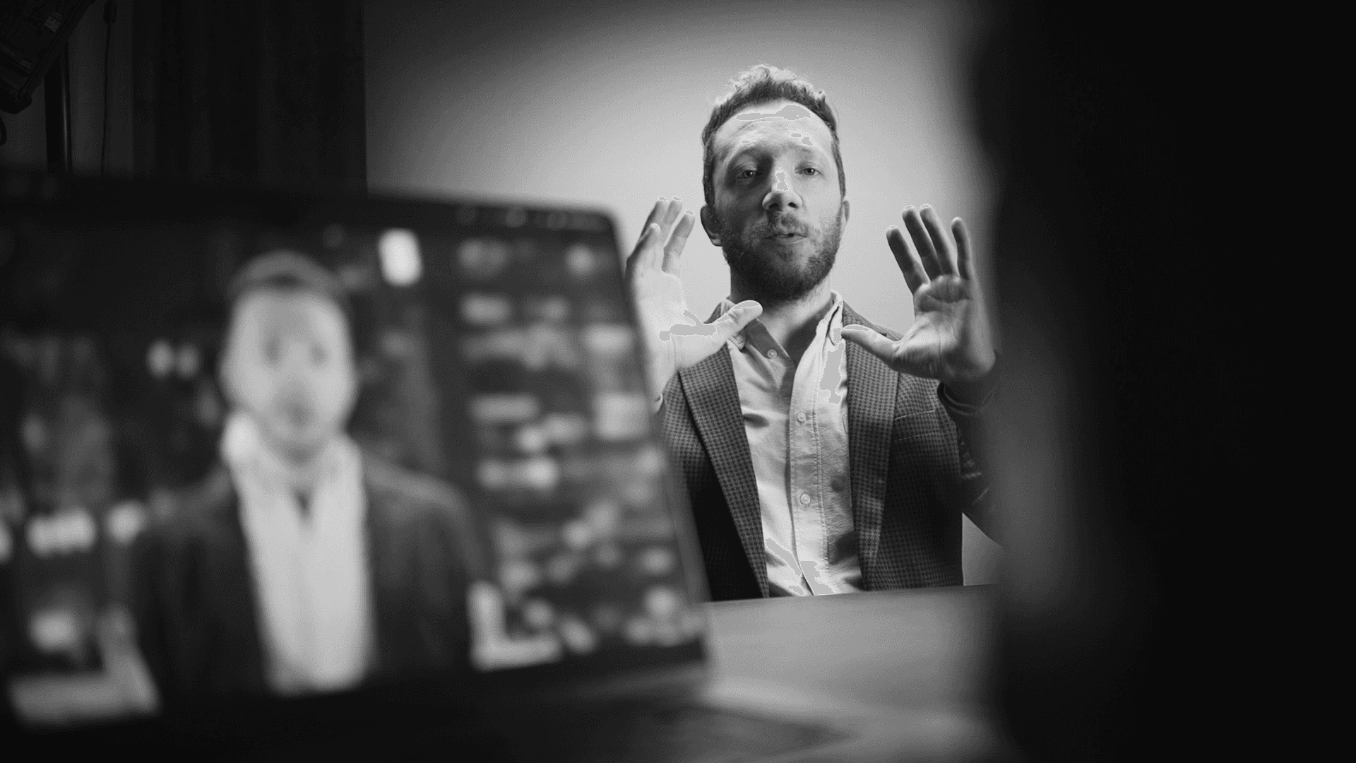 Black and white image of people working at a table with laptops, showing hands gesturing during discussion of digital content displayed on screens, with fabrica® logo in the corner.