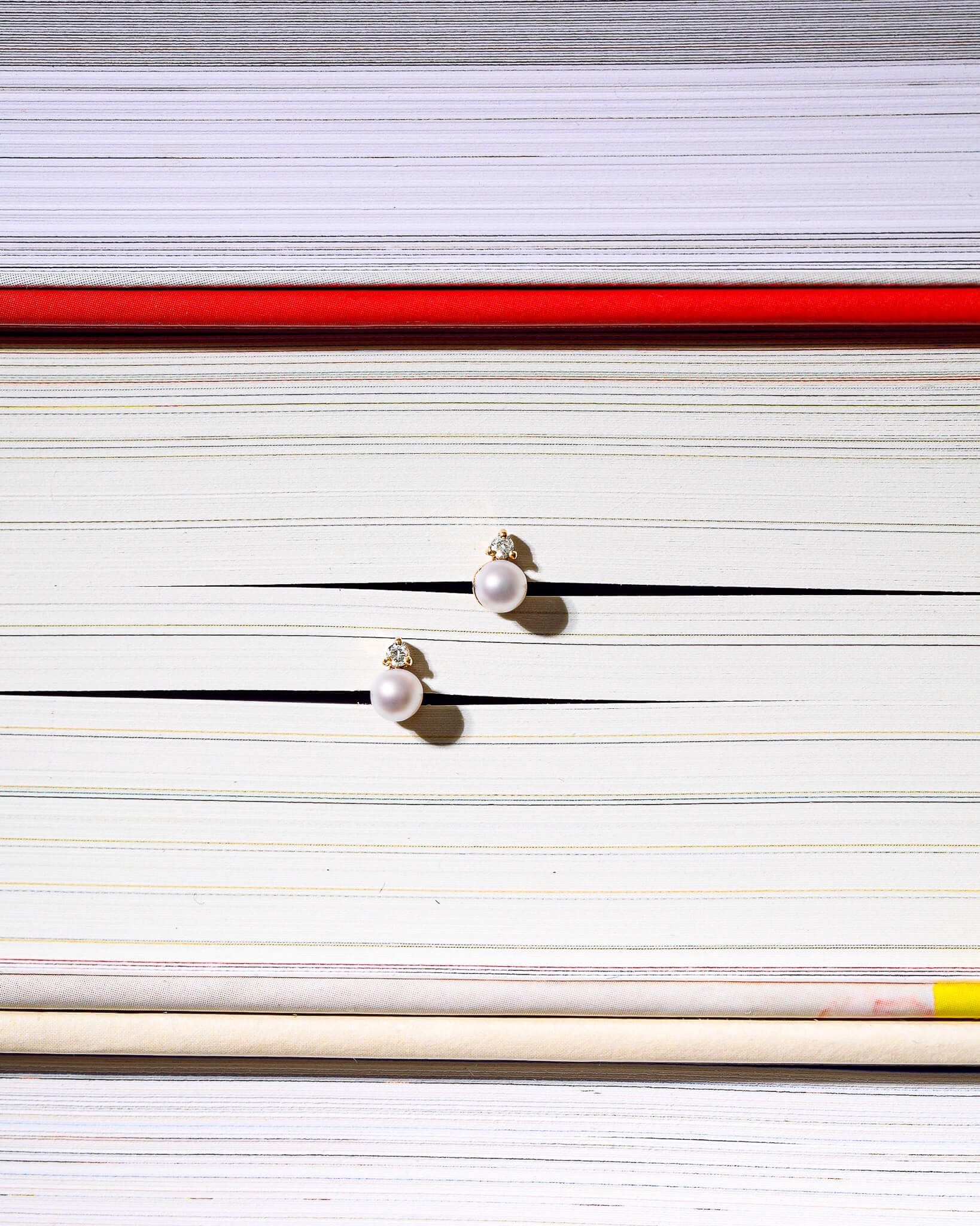 Pearl stud earrings styled on stacked books in editorial still-life composition.