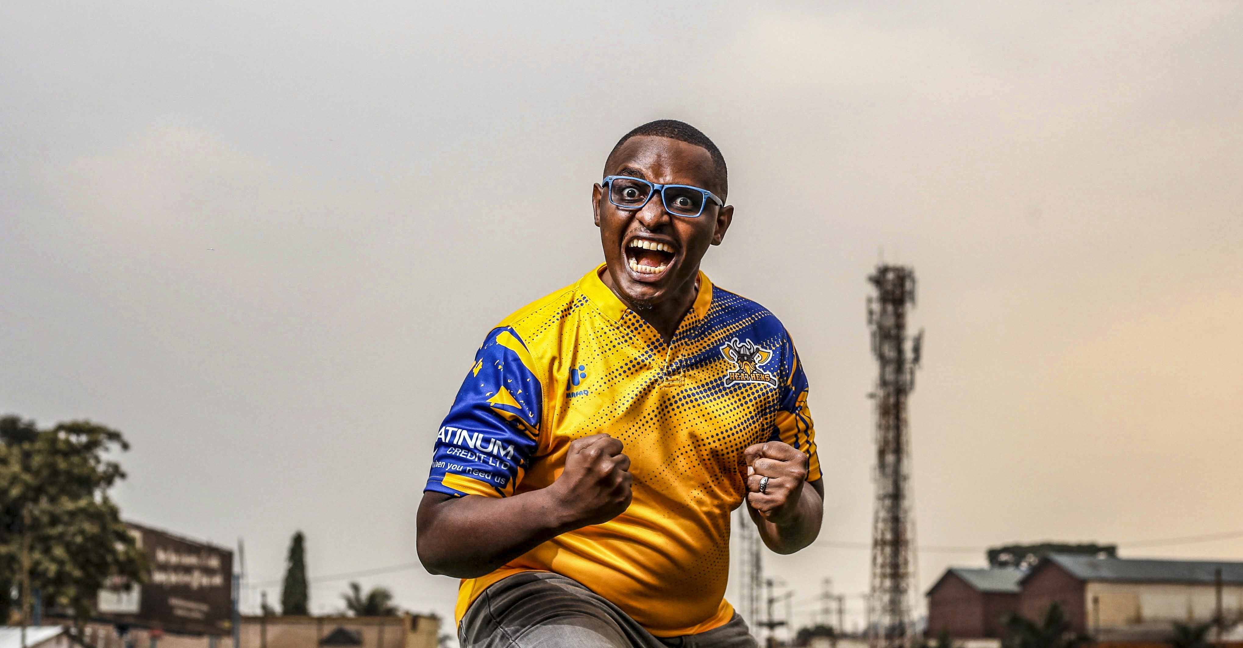 Man dressed in dark casual wear sitting alone in a stadium’s empty rows of purple chairs, lit by dramatic moody lighting.