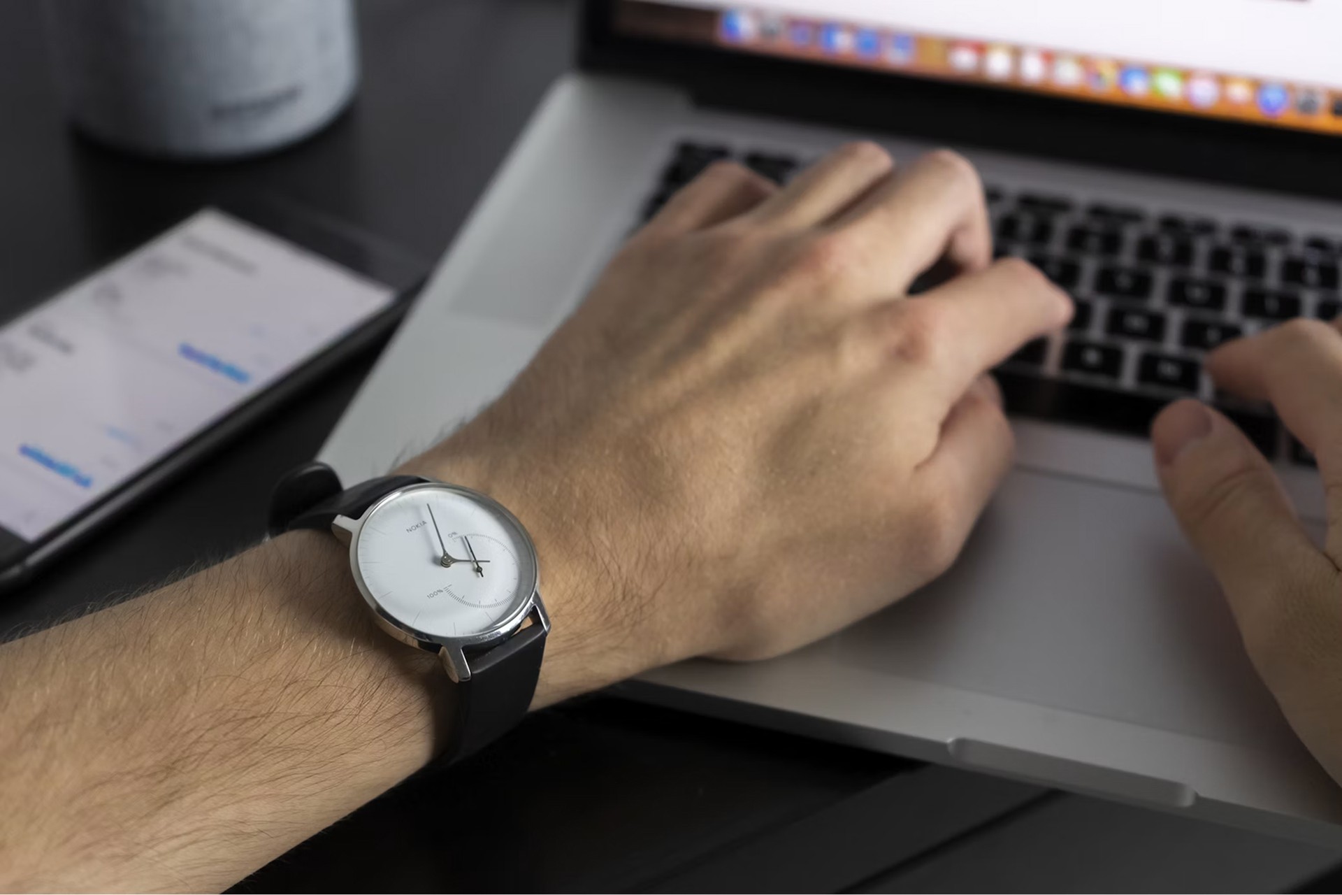 Person typing on a laptop with a smartphone and wristwatch nearby, representing mindful time management.