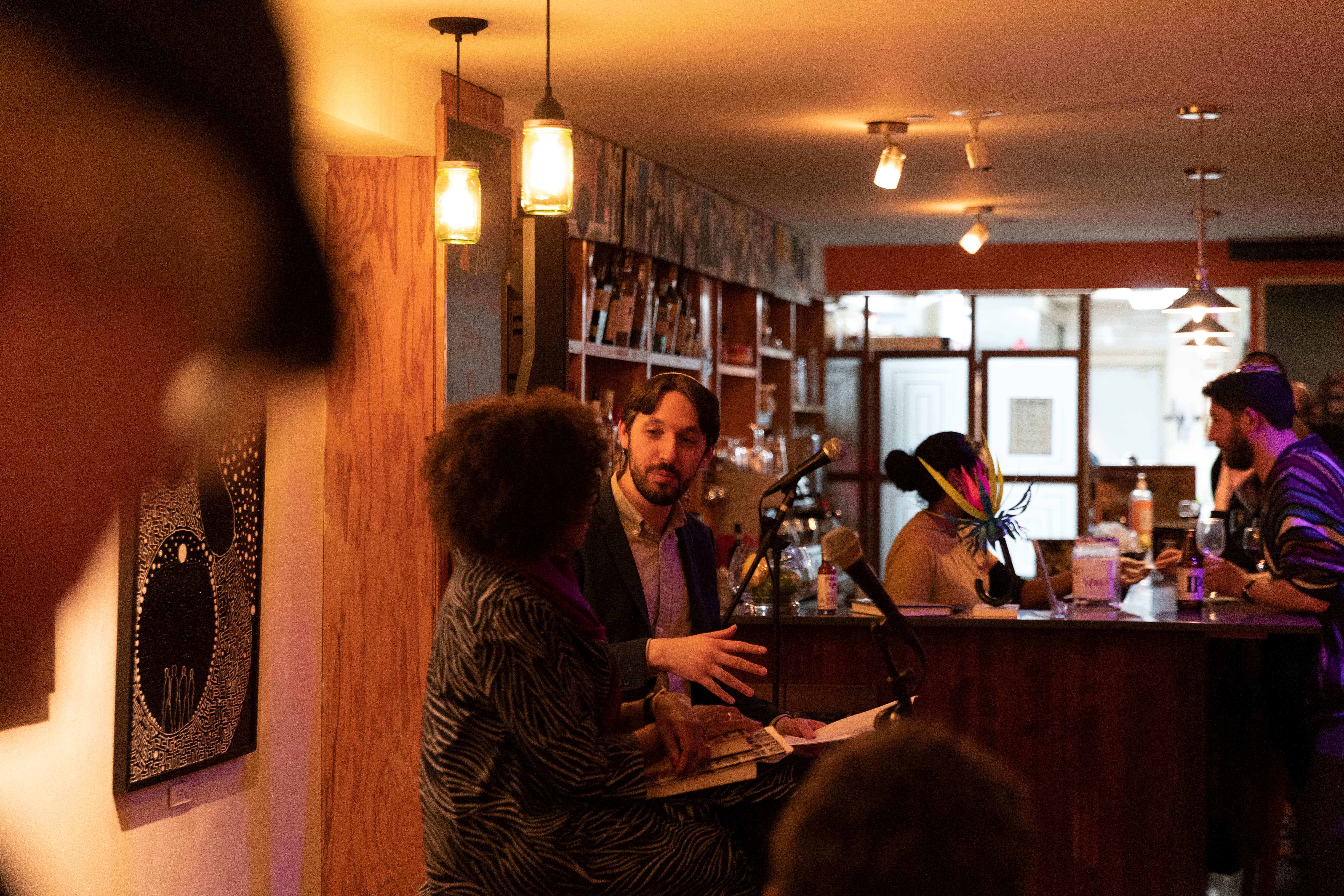 A group of people sitting around a coffee table on couches in a cozy, warmly lit space 