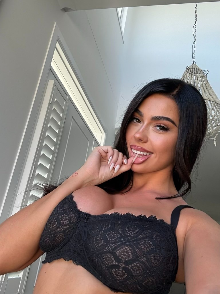 Topless waitress Valentina posing indoors in black lace lingerie, smiling for an Hourglass Gold Coast promotional photo.