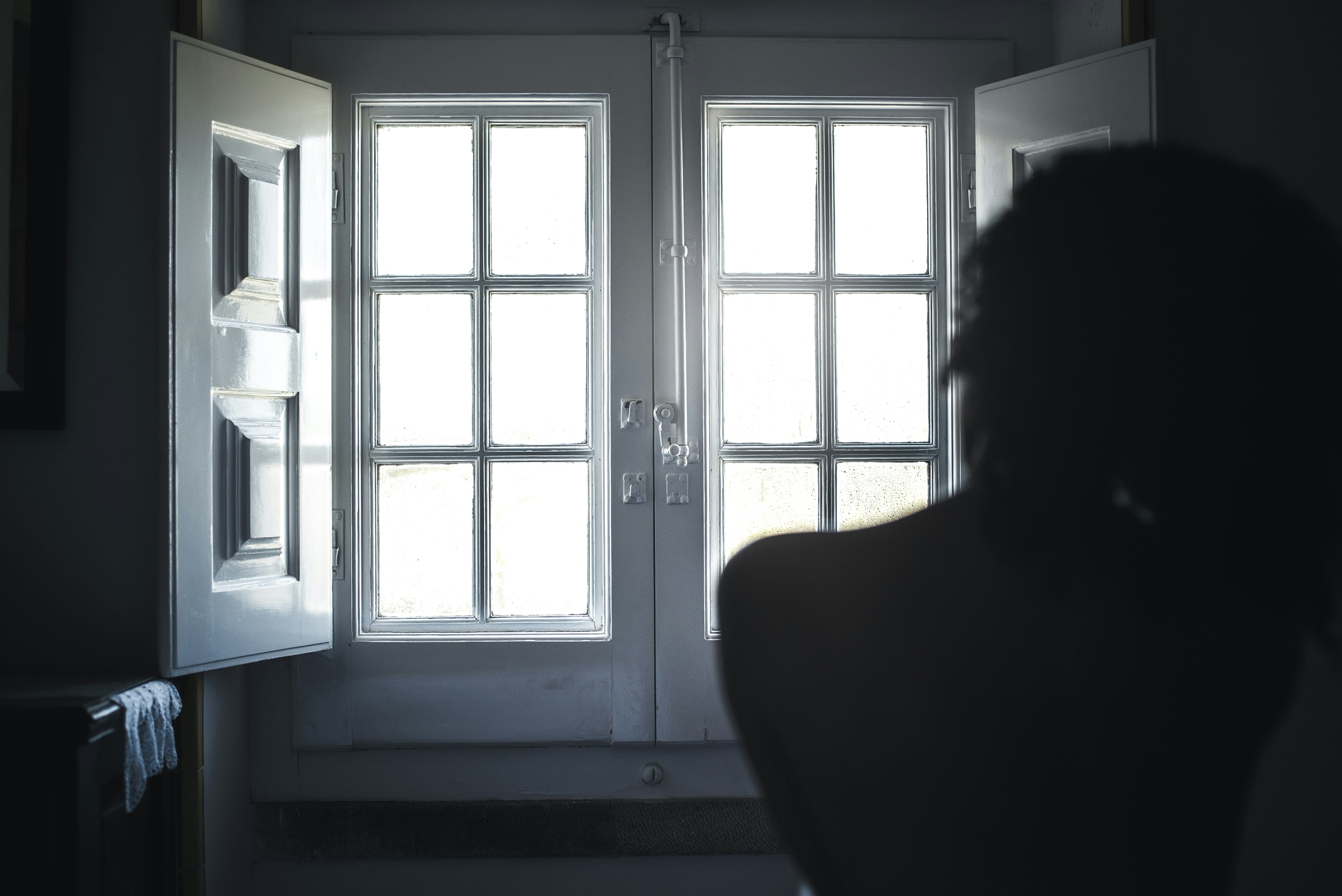 A woman looking toward a window as soft white sunlight enters the room.
