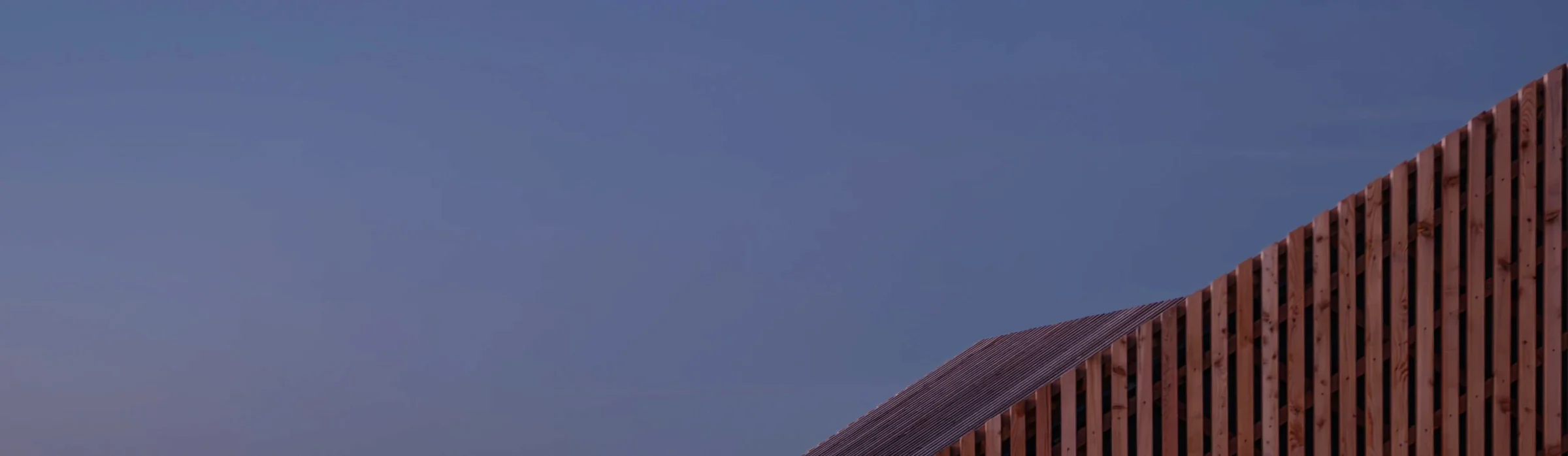 Dachkante aus Holzlatten steigt schräg in den violetten Abendhimmel