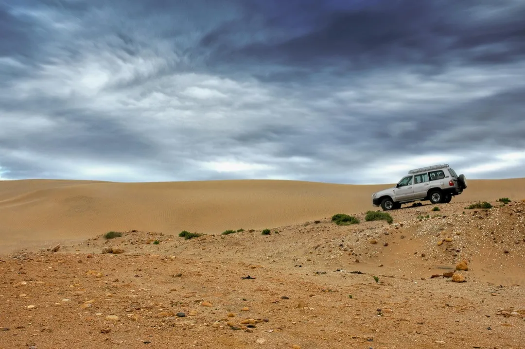 four wheel drive vehicle in a sandy landscape under dark, foreboding skies