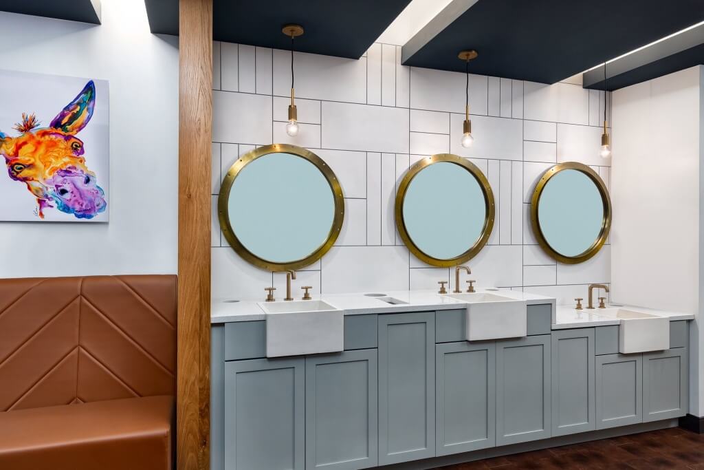 Three circular mirrors are mounted on a wall with a wooden bench below, featuring a playful mural nearby.