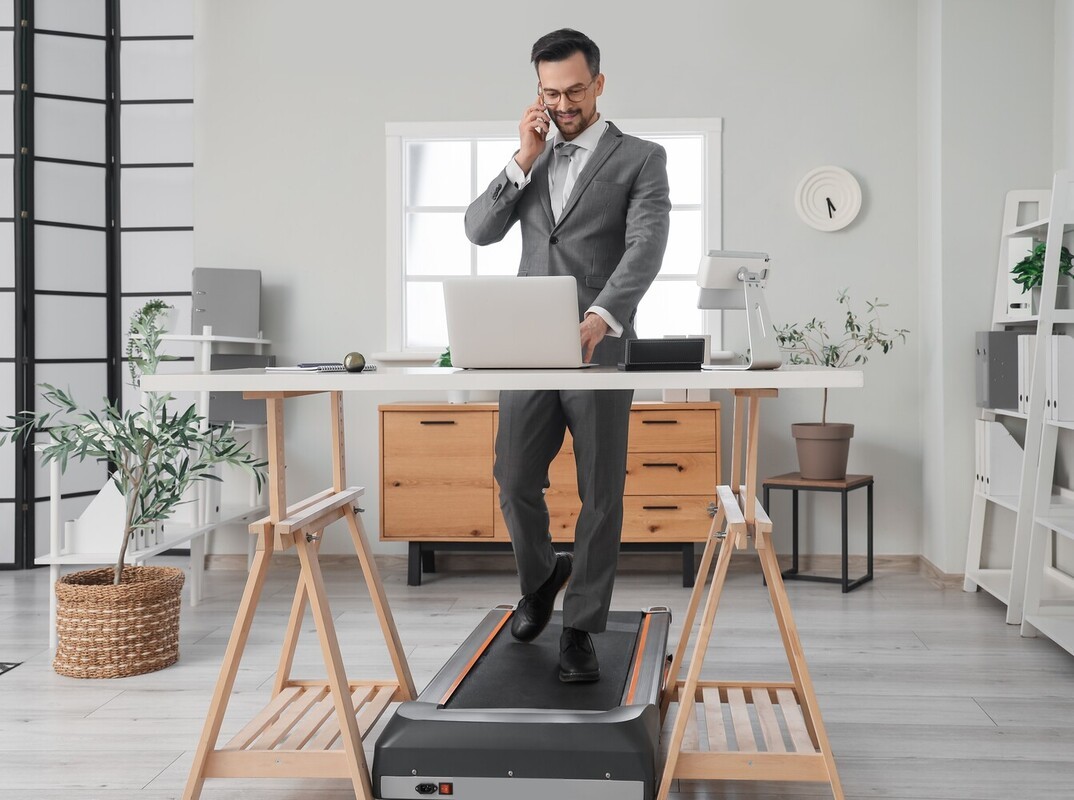“man using a desk treadmill in his home office for losing weight walking on treadmill while he does his job