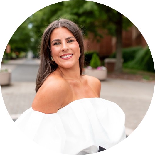Close-up portrait of a freckled woman with soft pink hair and star earring, natural light, white tank top.