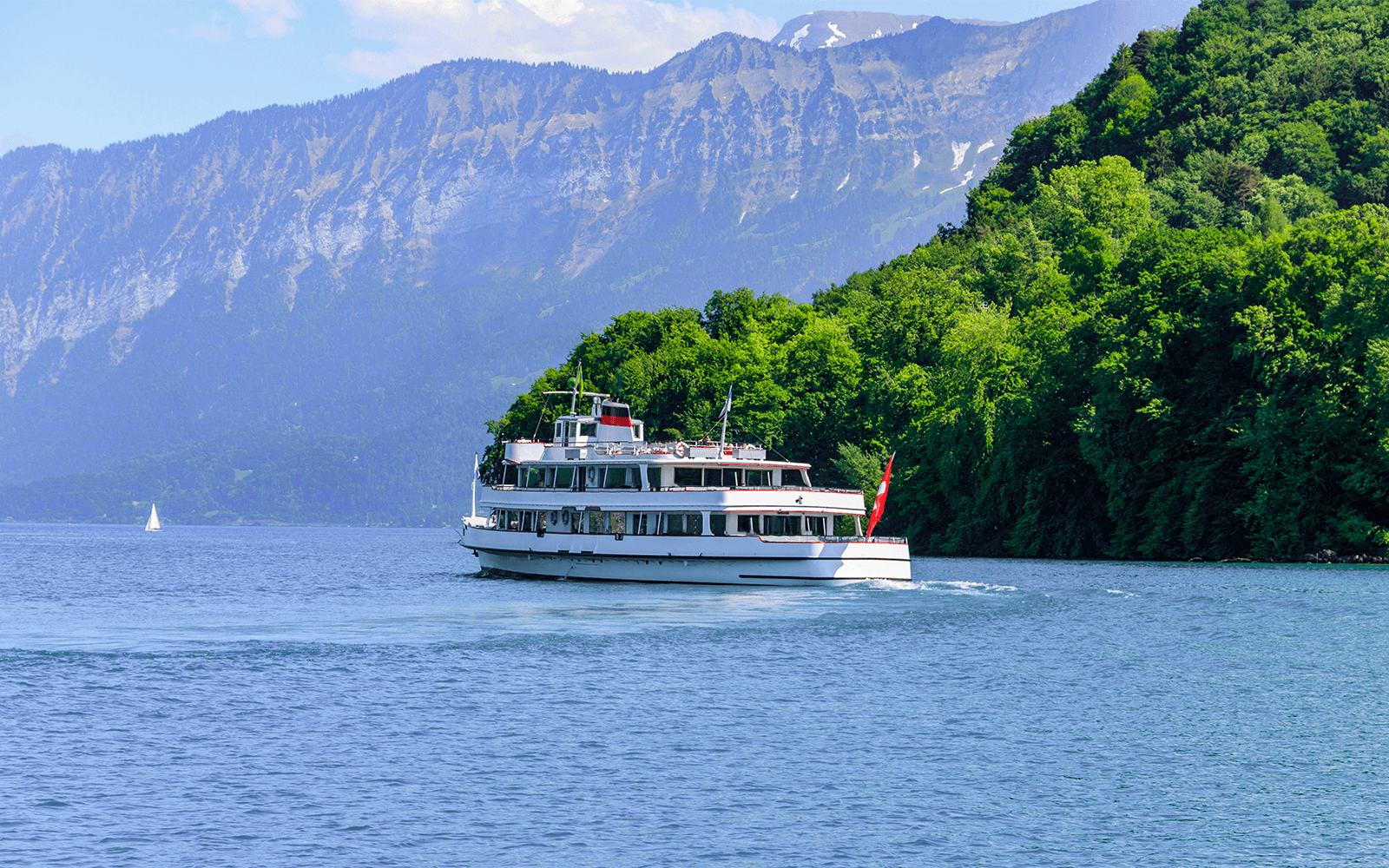 Passenger ship cruising on Lake Thun, Switzerland, with mountains in the background.