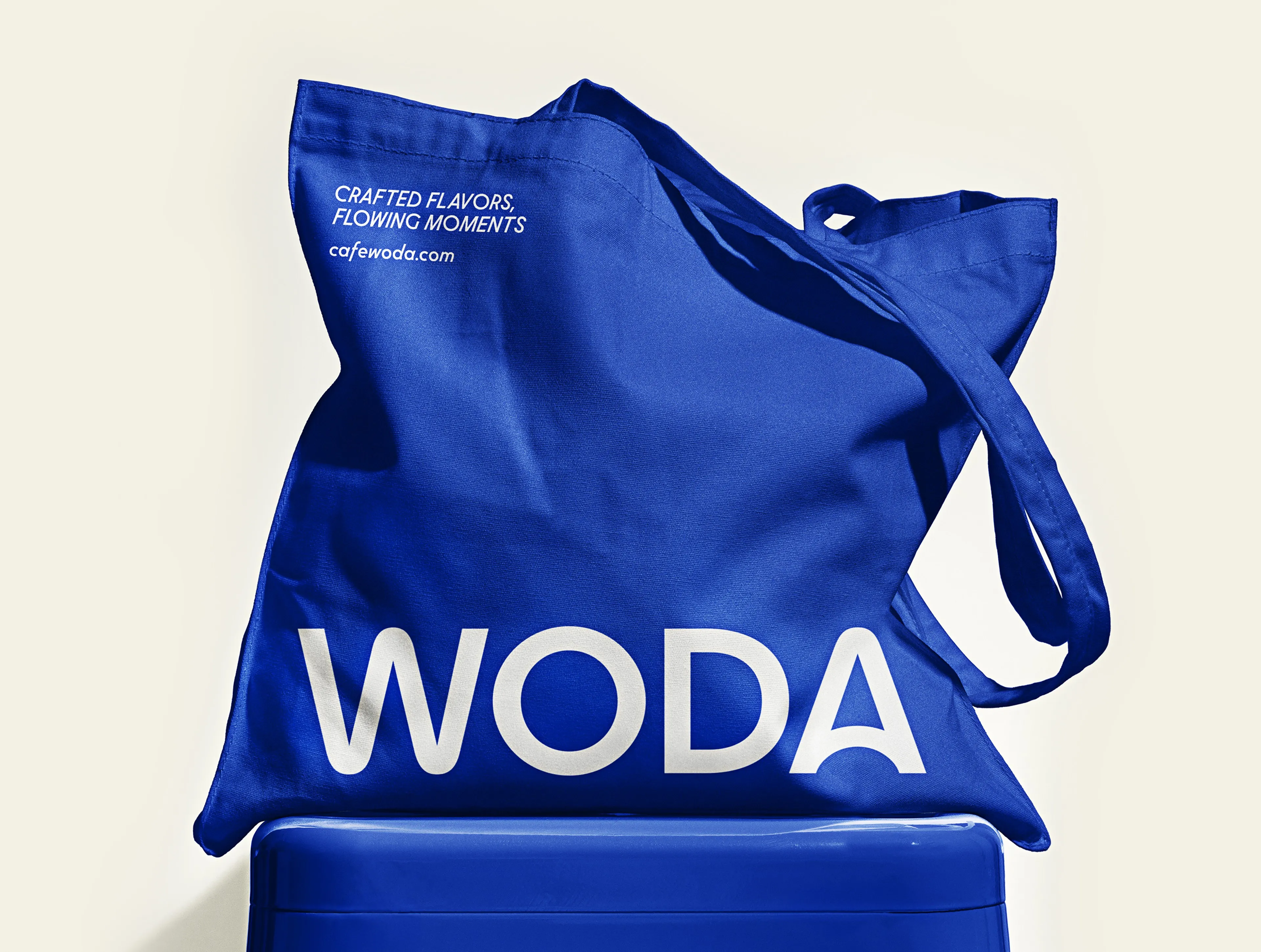 Royal blue Woda tote bag with white logotype and the slogan Crafted flavors, flowing moments, restaurant merchandise design
