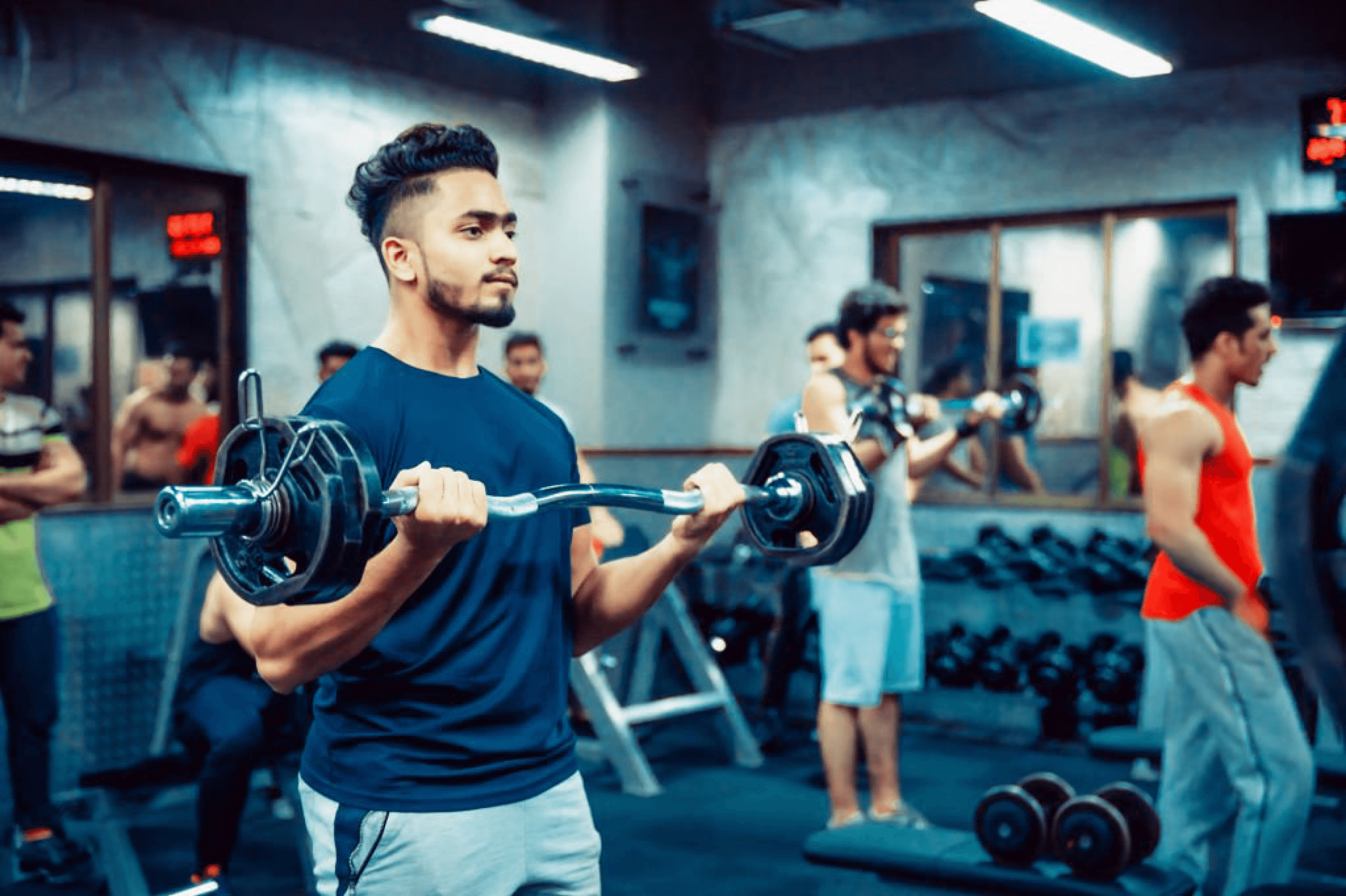 Young Indian man lifting weights in gym with others exercising in background