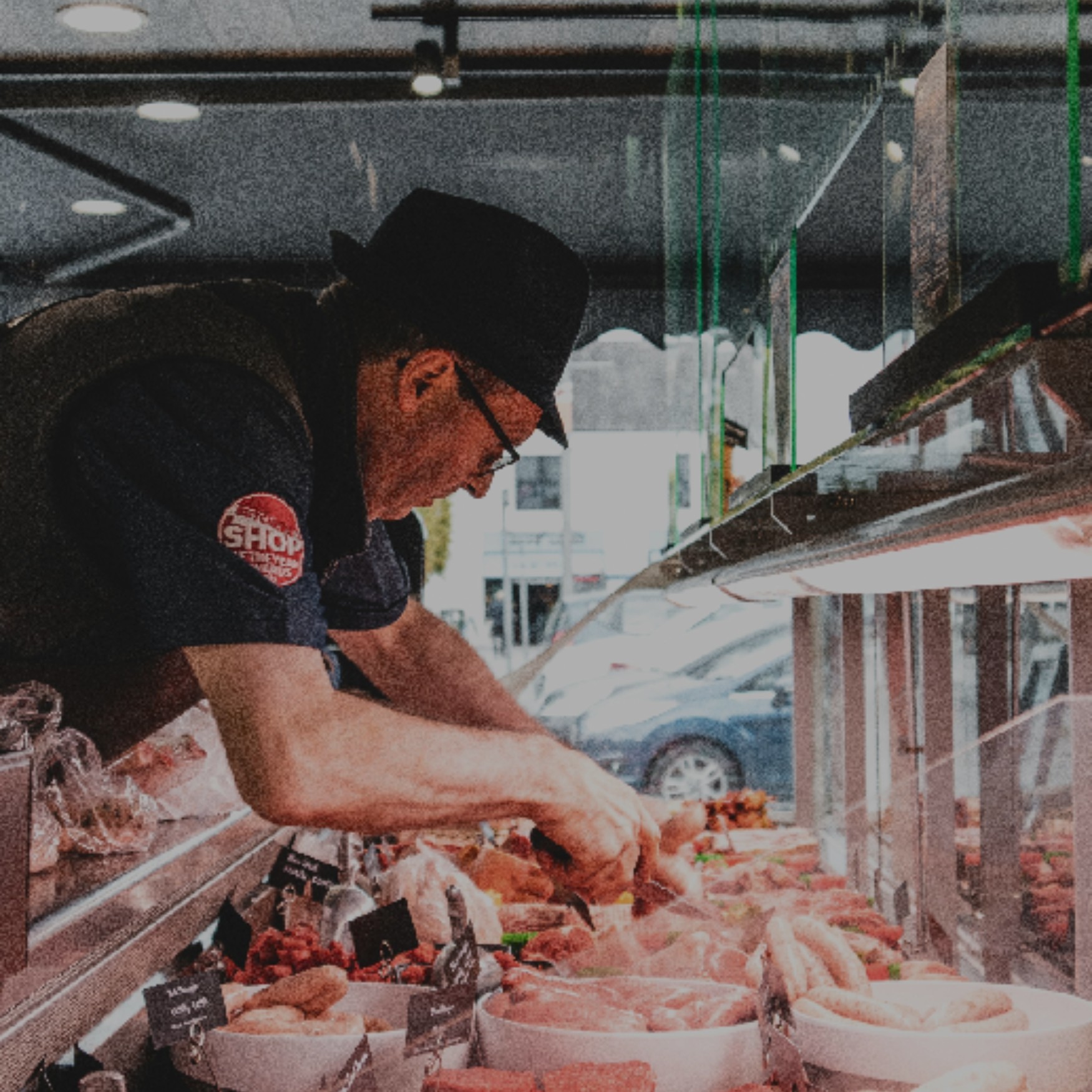 man in black crew neck t-shirt and black hat standing in front of raw meat