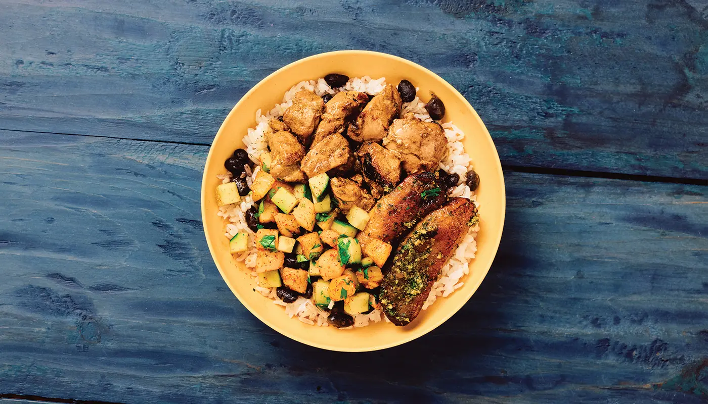 Overhead photograph of the original jerk chicken bowl in a yellow bowl on blue wooden boards.