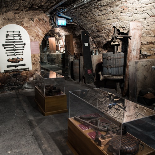 Historische Museumsausstellung in einem schwach beleuchteten Steinkeller, präsentiert alte Werkzeuge, Maschinen und Vitrinen mit Artefakten.