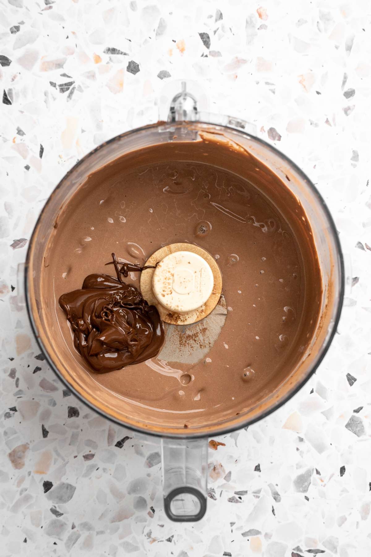 Adding melted chocolate to food processor with chocolate mousse.