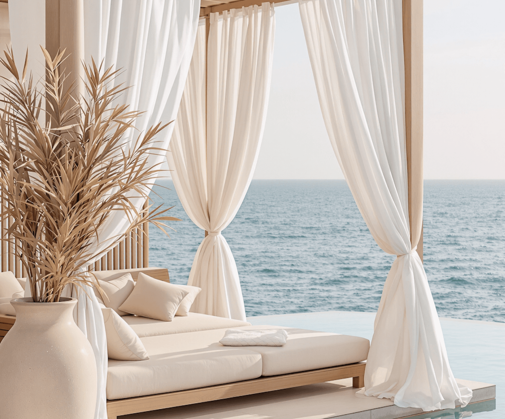 Luxurious poolside cabana with beige loungers, white drapes, and ocean view..