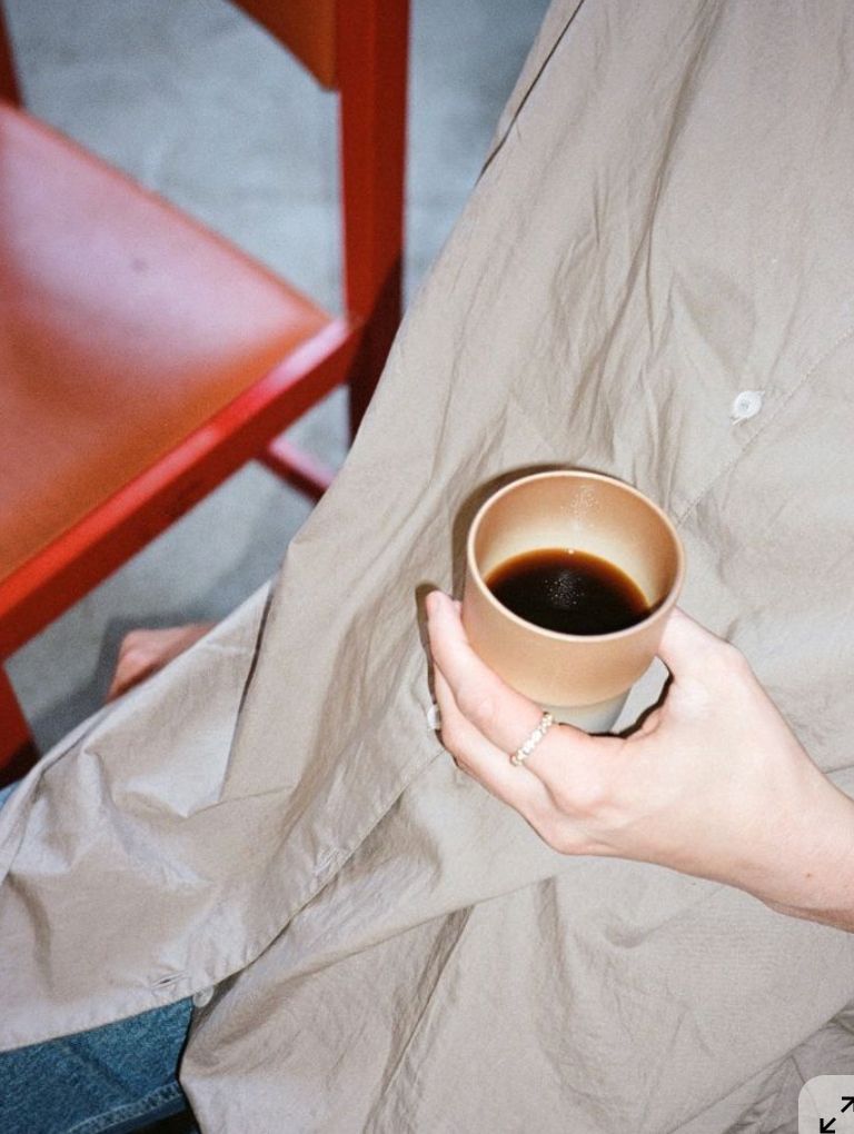 White plate with roasted carrots served on green sauce, topped with almonds and fresh herbs, held by a hand over a dark table.