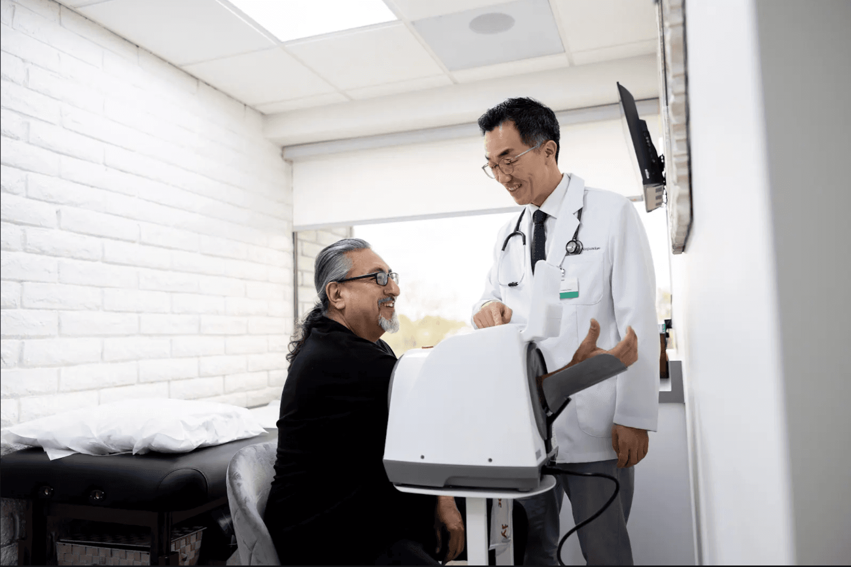 A male doctor in a white coat providing guidance to a patient using an InBody professional blood pressure monitor in a modern medical consultation room.