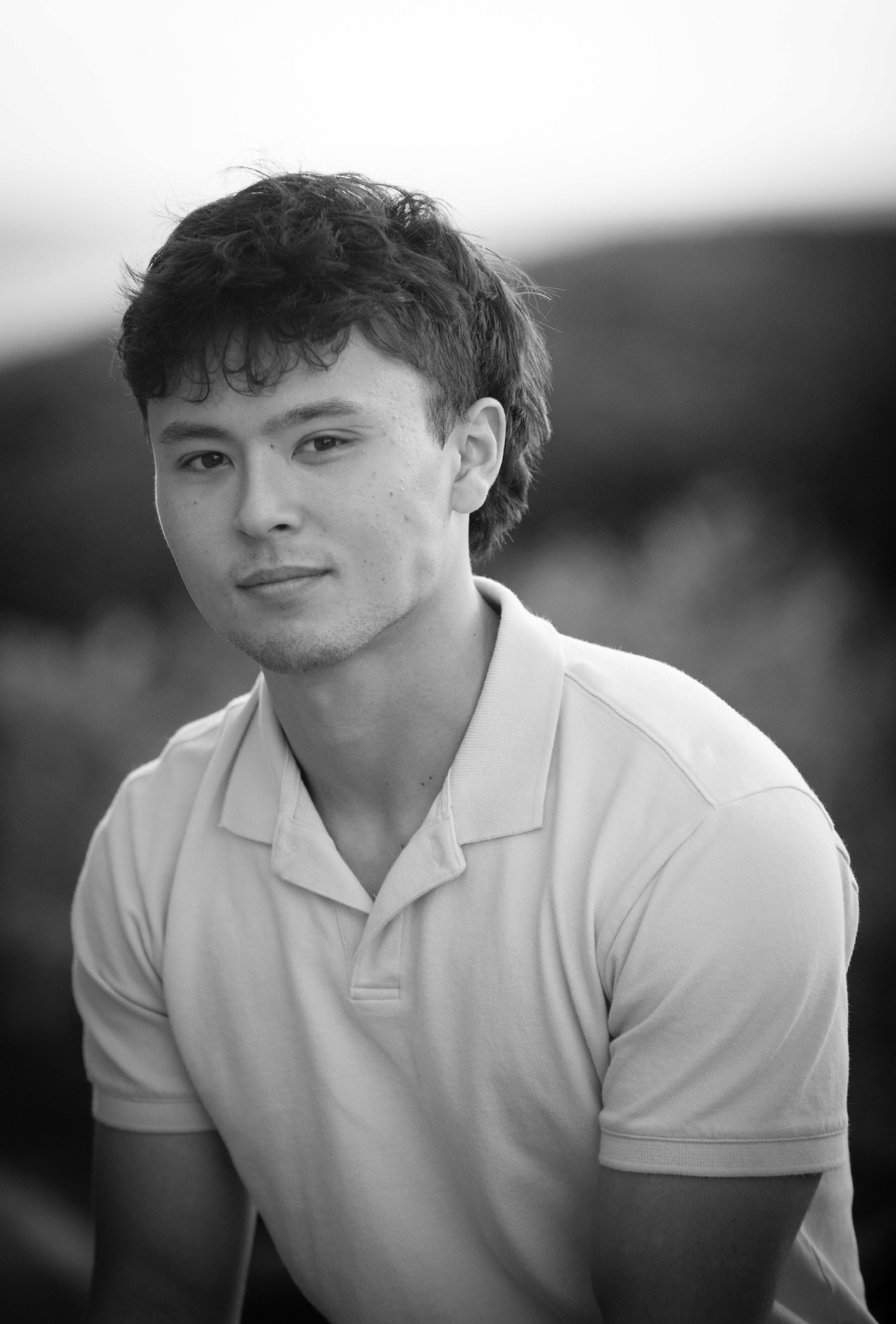Portrait of a young man with short hair, wearing a dark t-shirt, against a plain background.