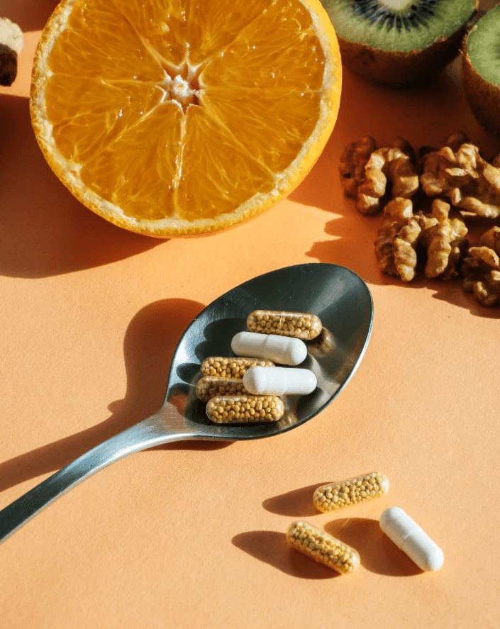 Supplement capsules on spoon with orange, kiwi and walnuts in background