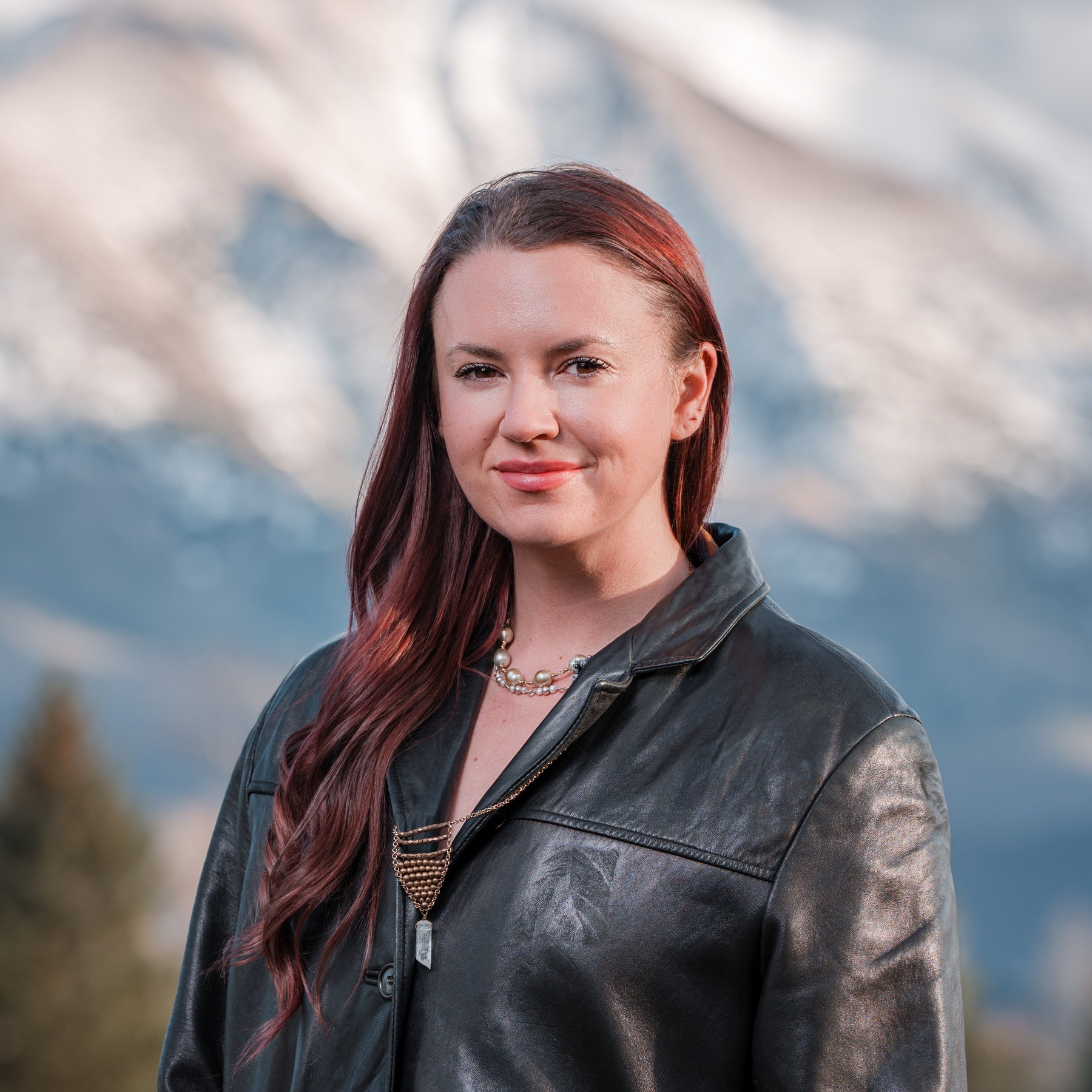 Woman in a black leather jacket photographed for a headshot with snowy mountains behind her