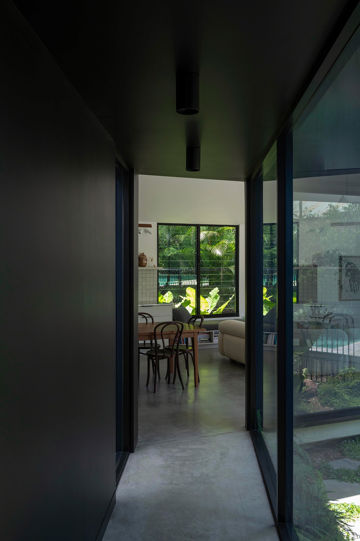 Interior hallway at Toohey Forest House with glazed wall overlooking courtyard and views through to living and dining areas.
