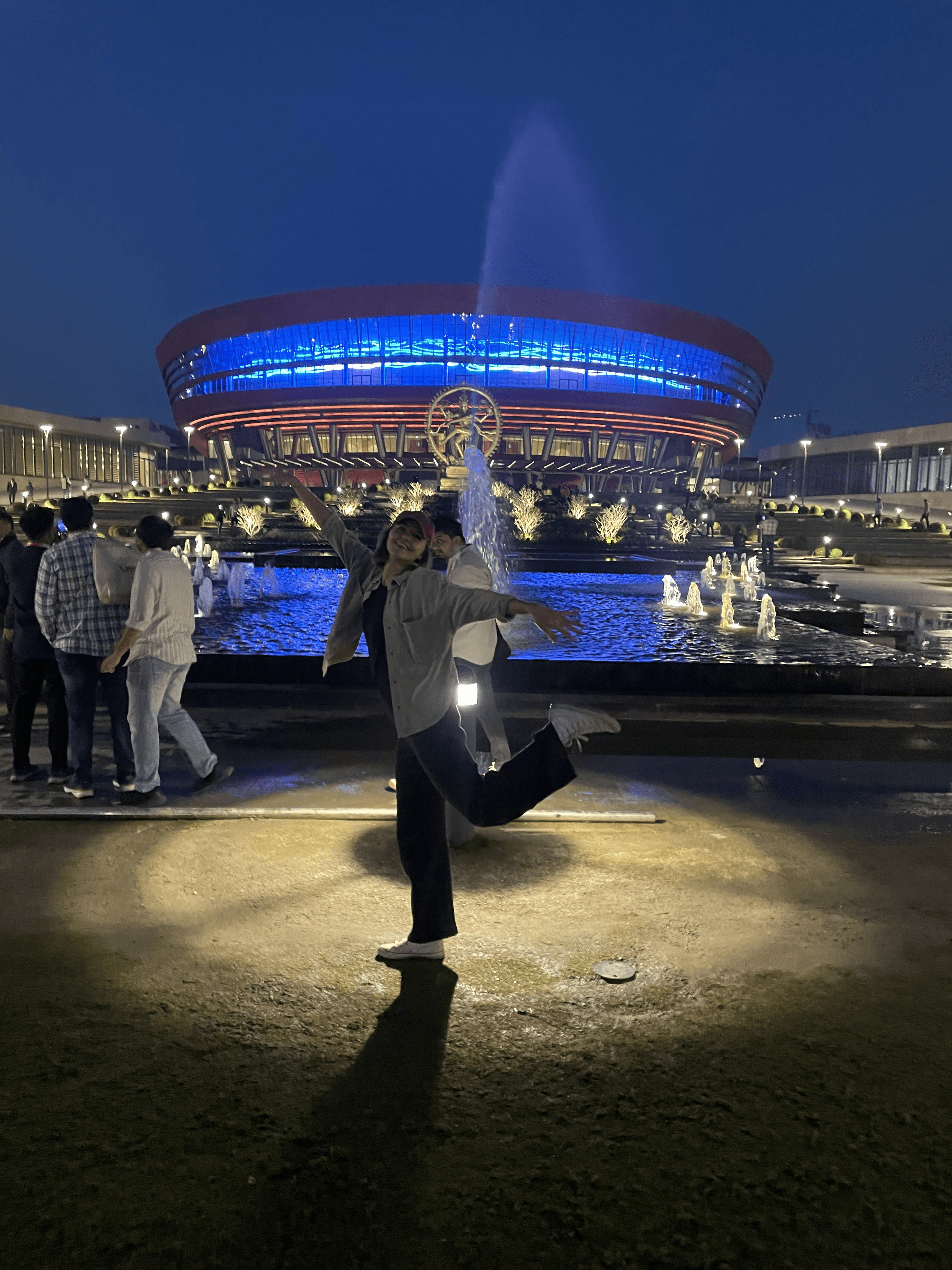 Me smiling at night by lit-up Bharat Tex Summit with blue lights.