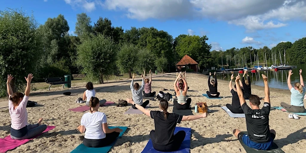 Gruppe entspannt bei einer Yoga-Session am Dranländersee und genießt danach ein gesundes Picknick; Strong Partners zeigt praxisnah Betriebliches Gesundheitsmanagement für mehr Wohlbefinden und Teamgesundheit im Unternehmen.