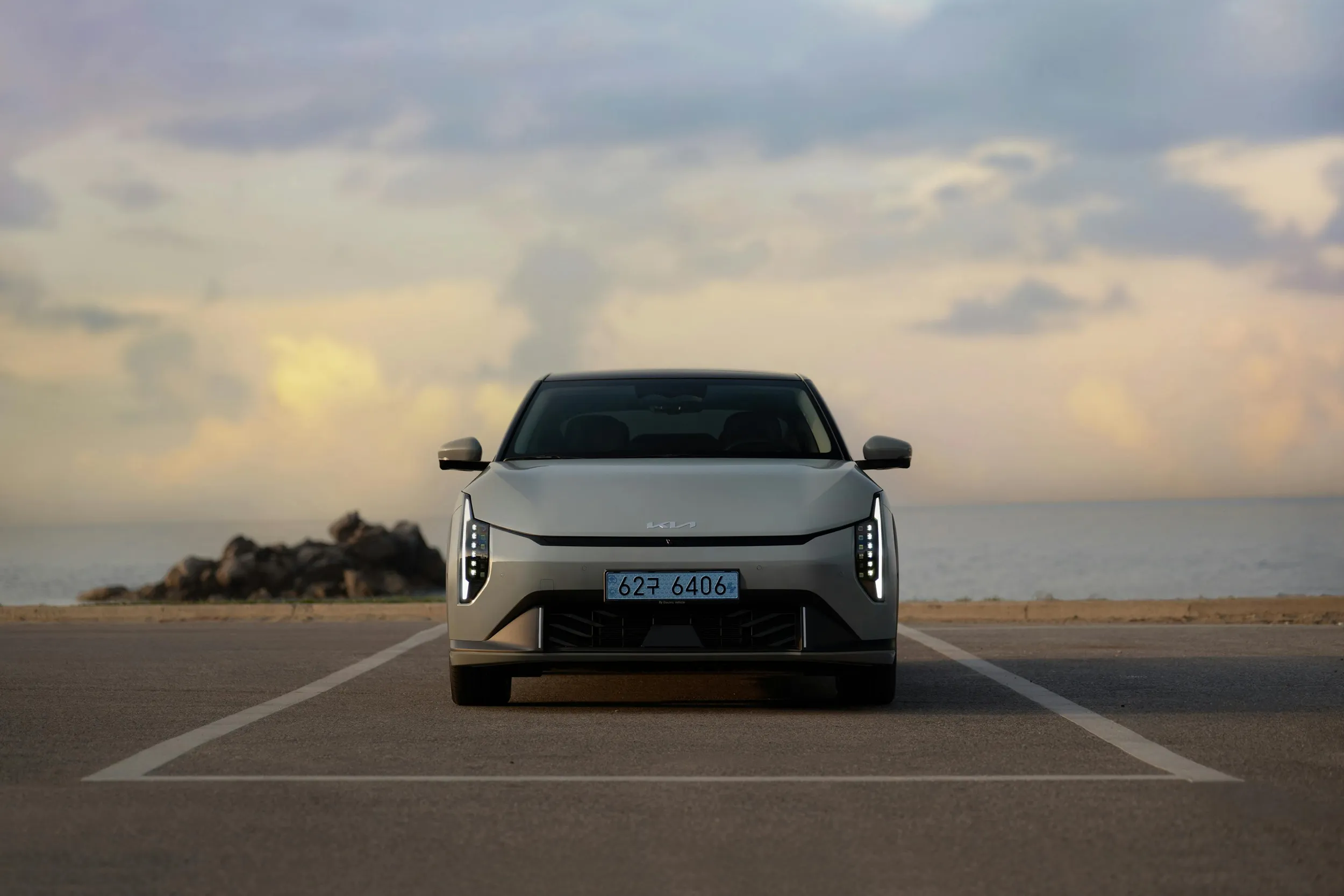Front view of modern electric sedan parked near seaside under dramatic sky