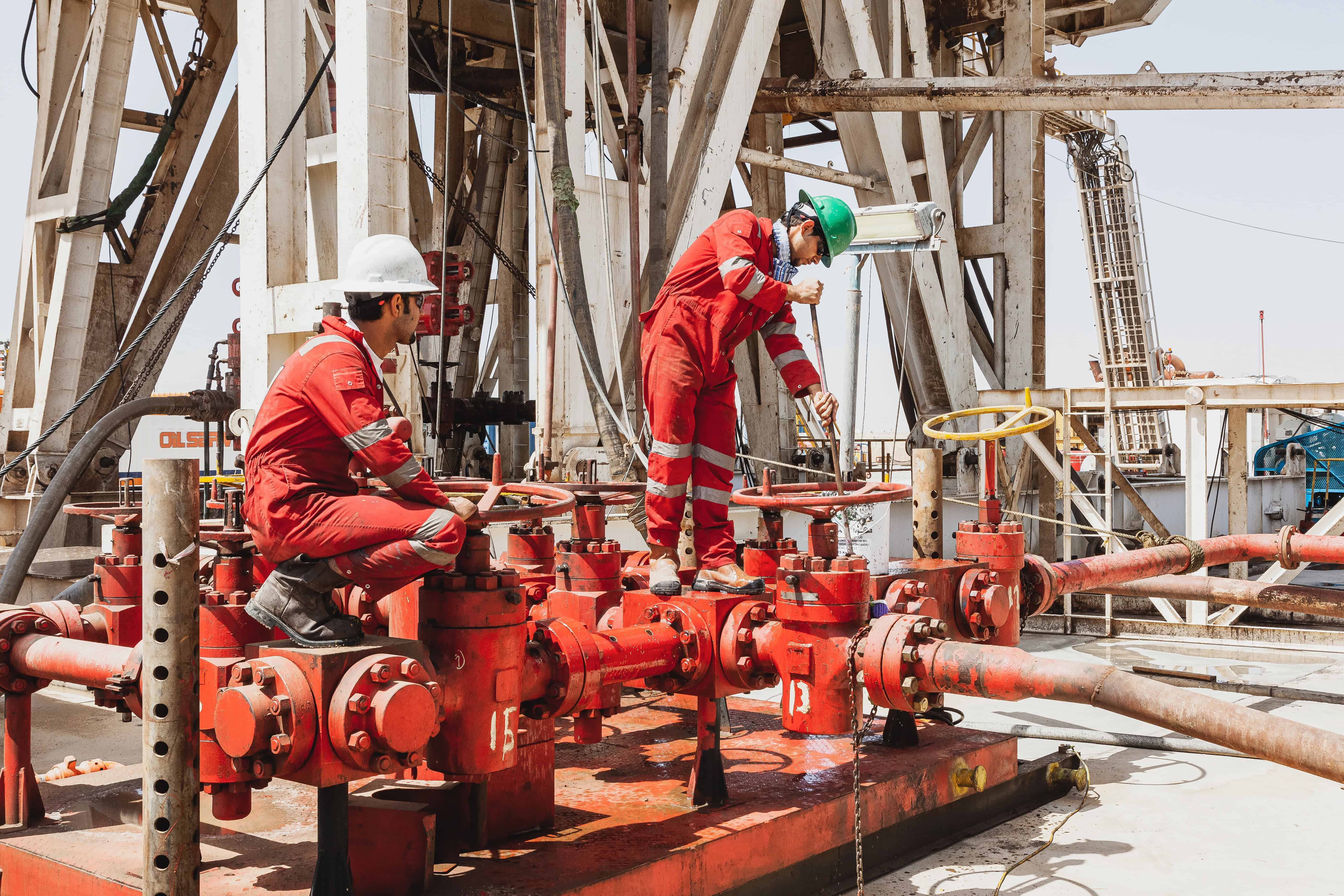 Oil rig workers in coveralls opening pipes at manifold using correct body positioning