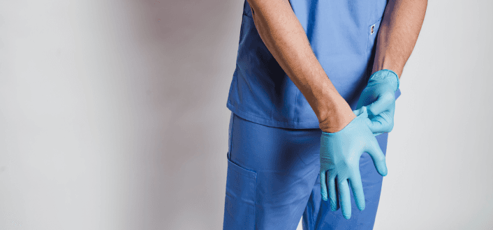 Healthcare worker in scrubs putting on disposable medical gloves.