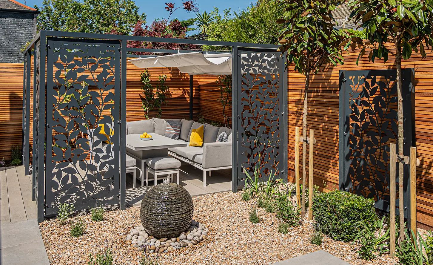 A garden entrance with decorative gates, potted plants, and a stone feature in a sunny outdoor setting.