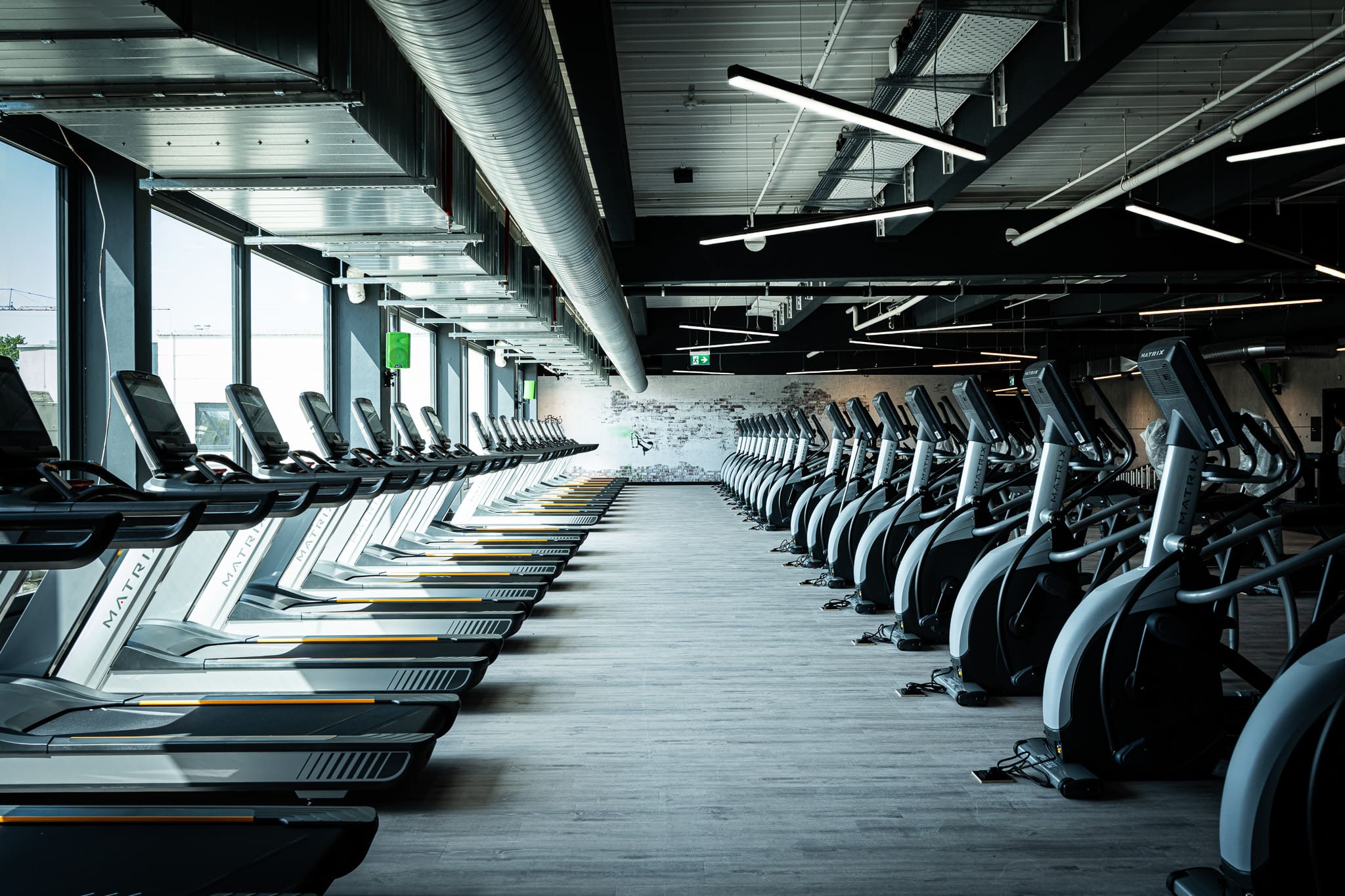 Moderne Sitzmöglichkeiten im XTRAFIT Fitnessstudio in Wiesbaden mit grünen Sitzmöglichkeiten, heller Beleuchtung und einem großen LED-Bildschirm.