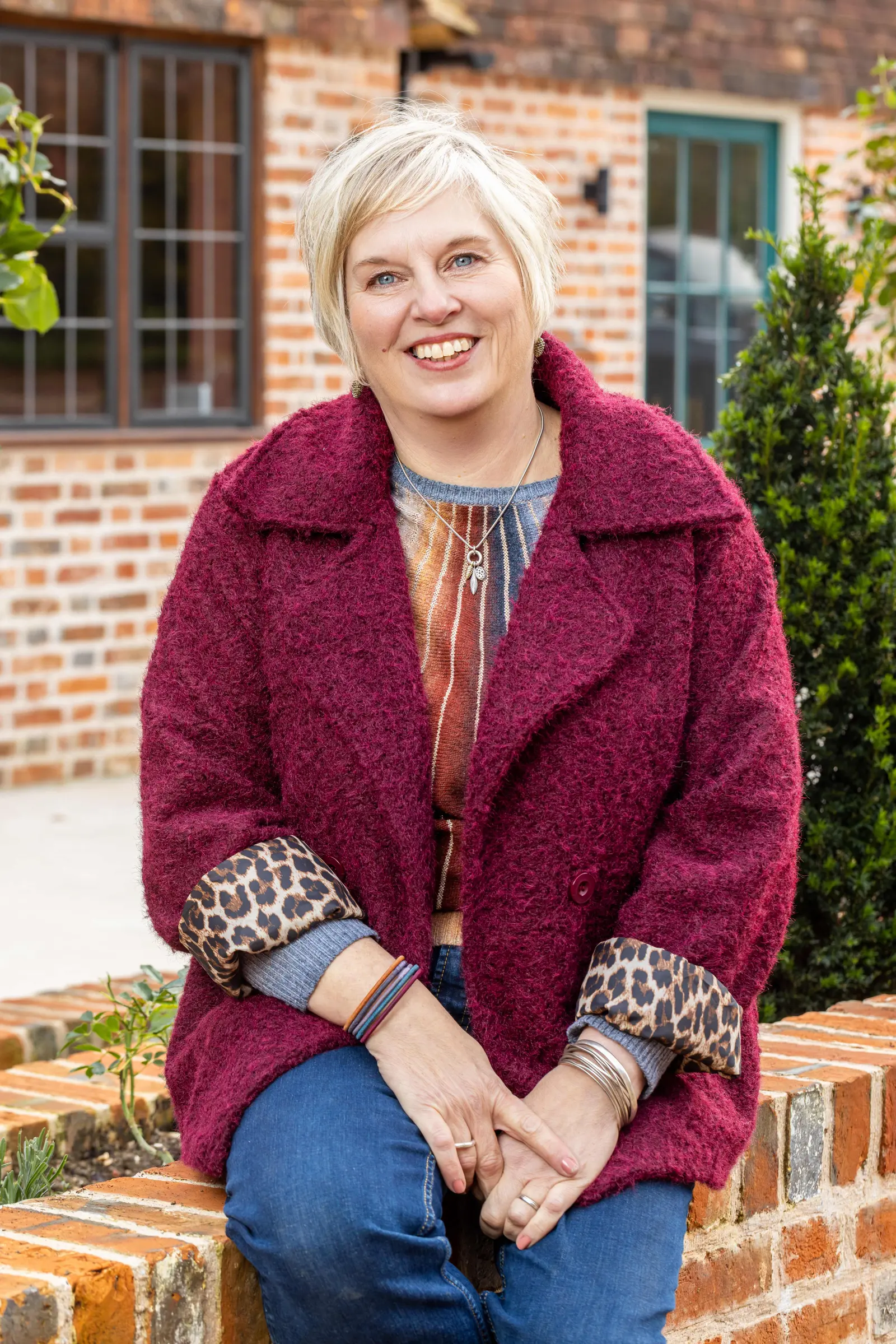 A smiling person sits outdoors on a red brick wall.