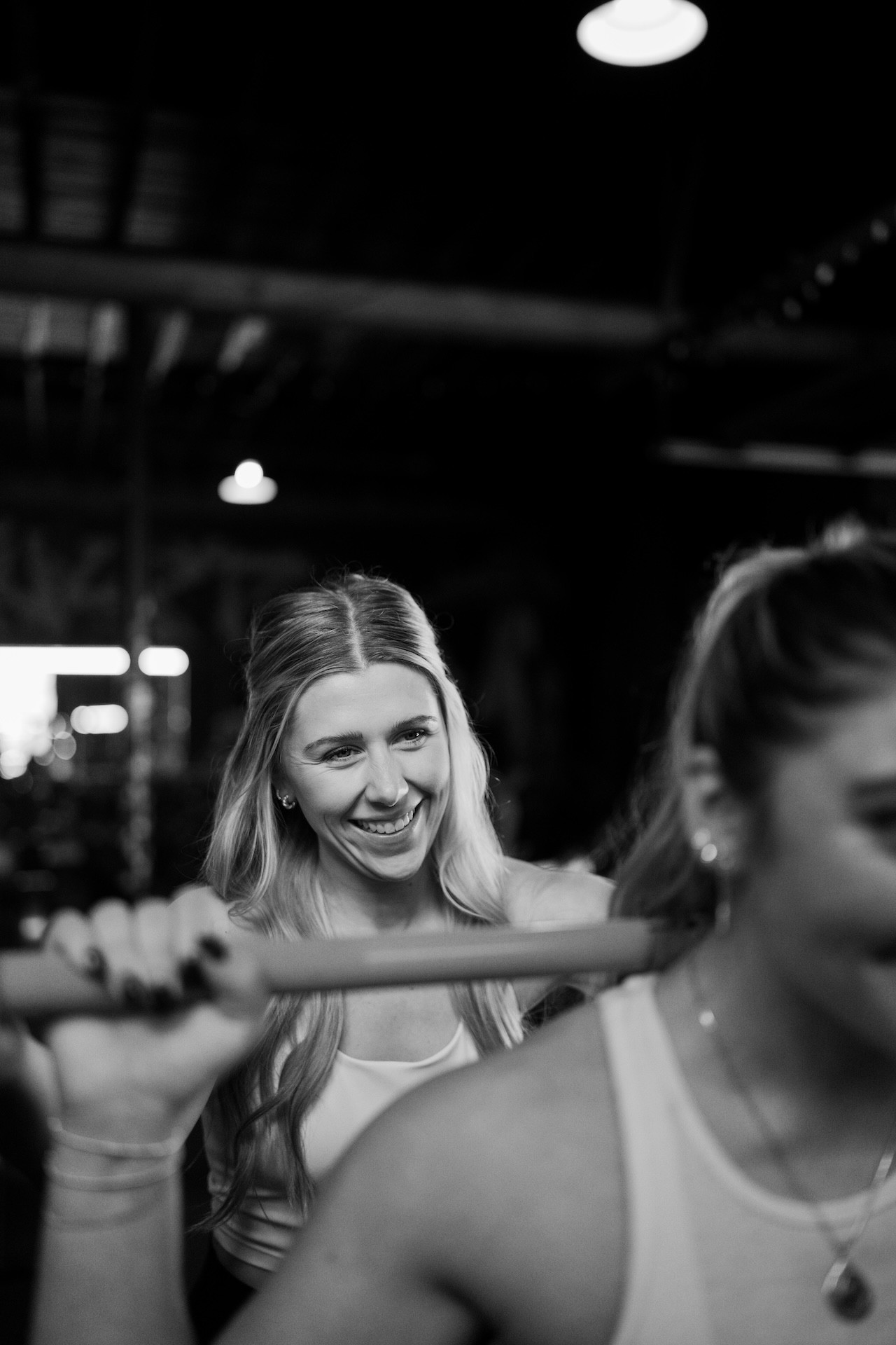 Personal trainer smiling while helping a woman barbell back squat