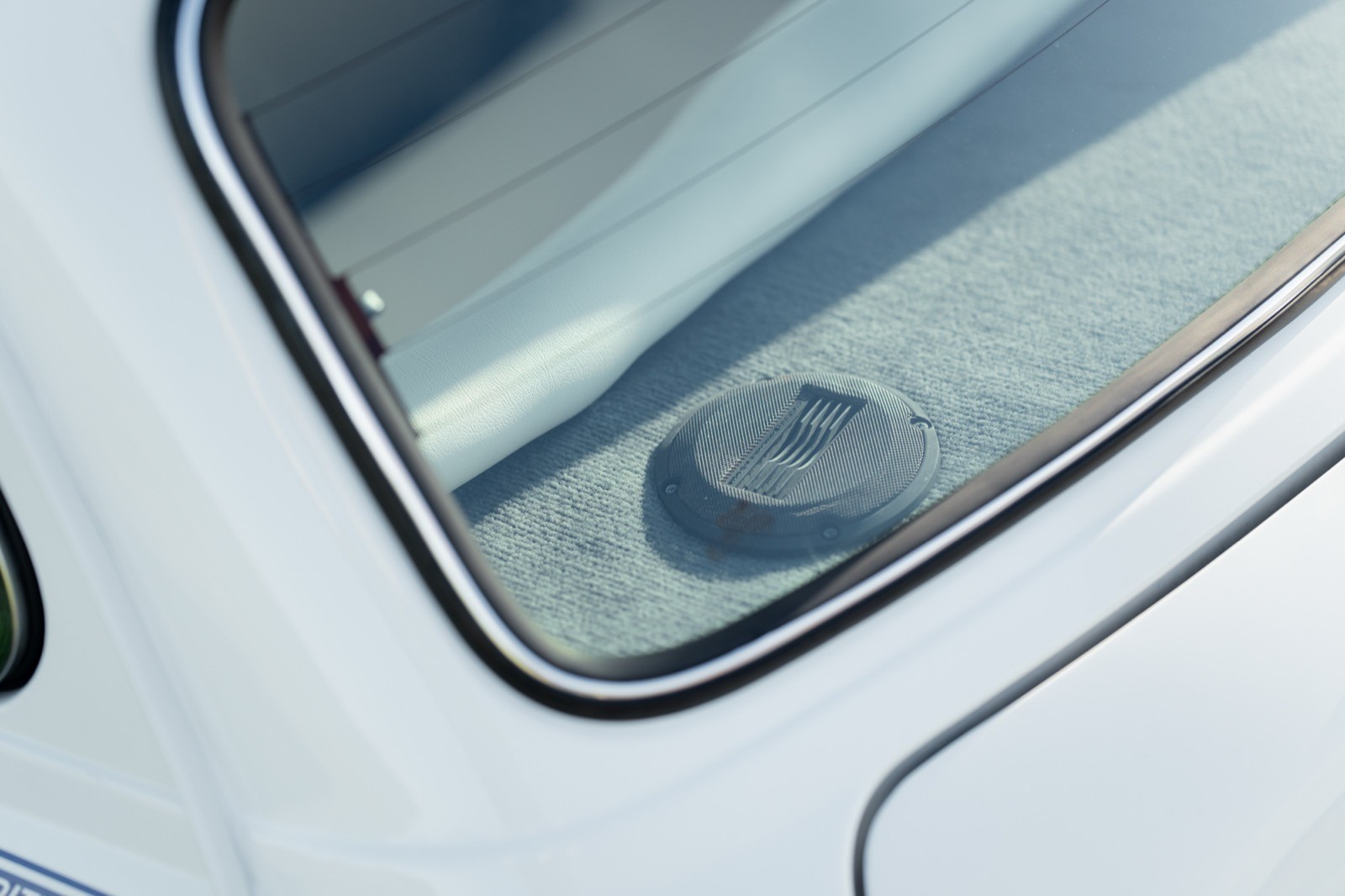Close-up of a car window showing the edge of the glass and a circular detail, reflecting light.