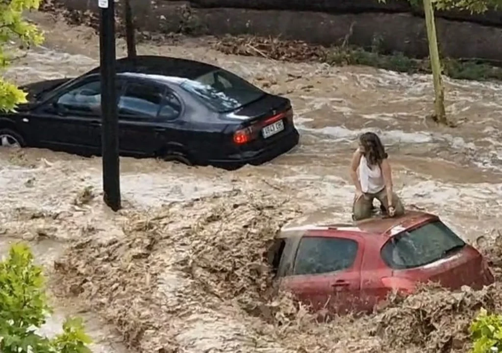 Imagen de la inundación del 6 de julio de 2023 en Zaragoza con una refugiandose de la corriente de agua sobre un coche