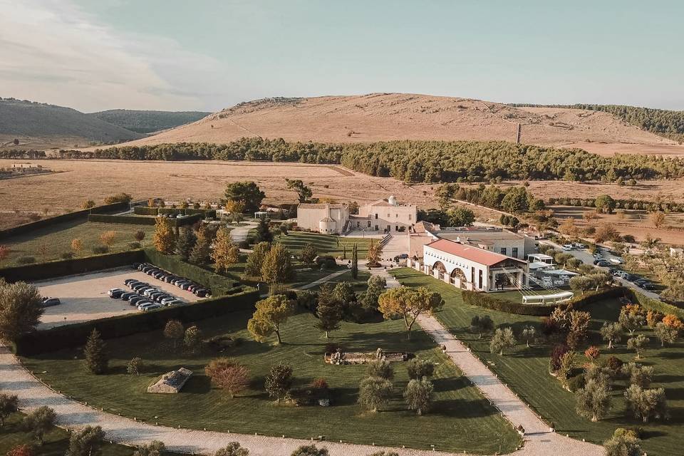 An elegant wedding ceremony setup features a domed gazebo adorned with peach and pink floral arrangements and lush greenery. White chairs line the aisle.