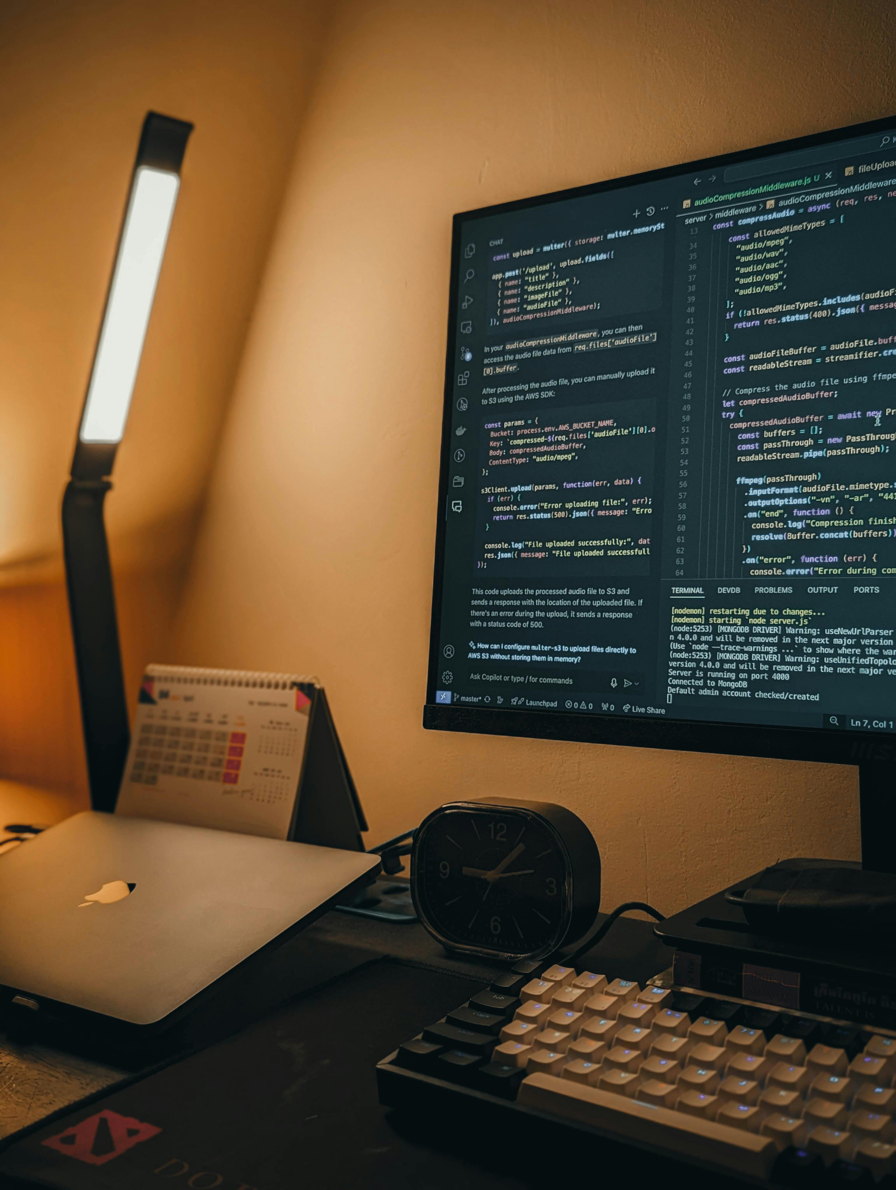 Scrivania con monitor, laptop e tastiera retroilluminata, con codice visibile sullo schermo, simbolo di lavoro da sviluppatore o formazione in ambito tech.